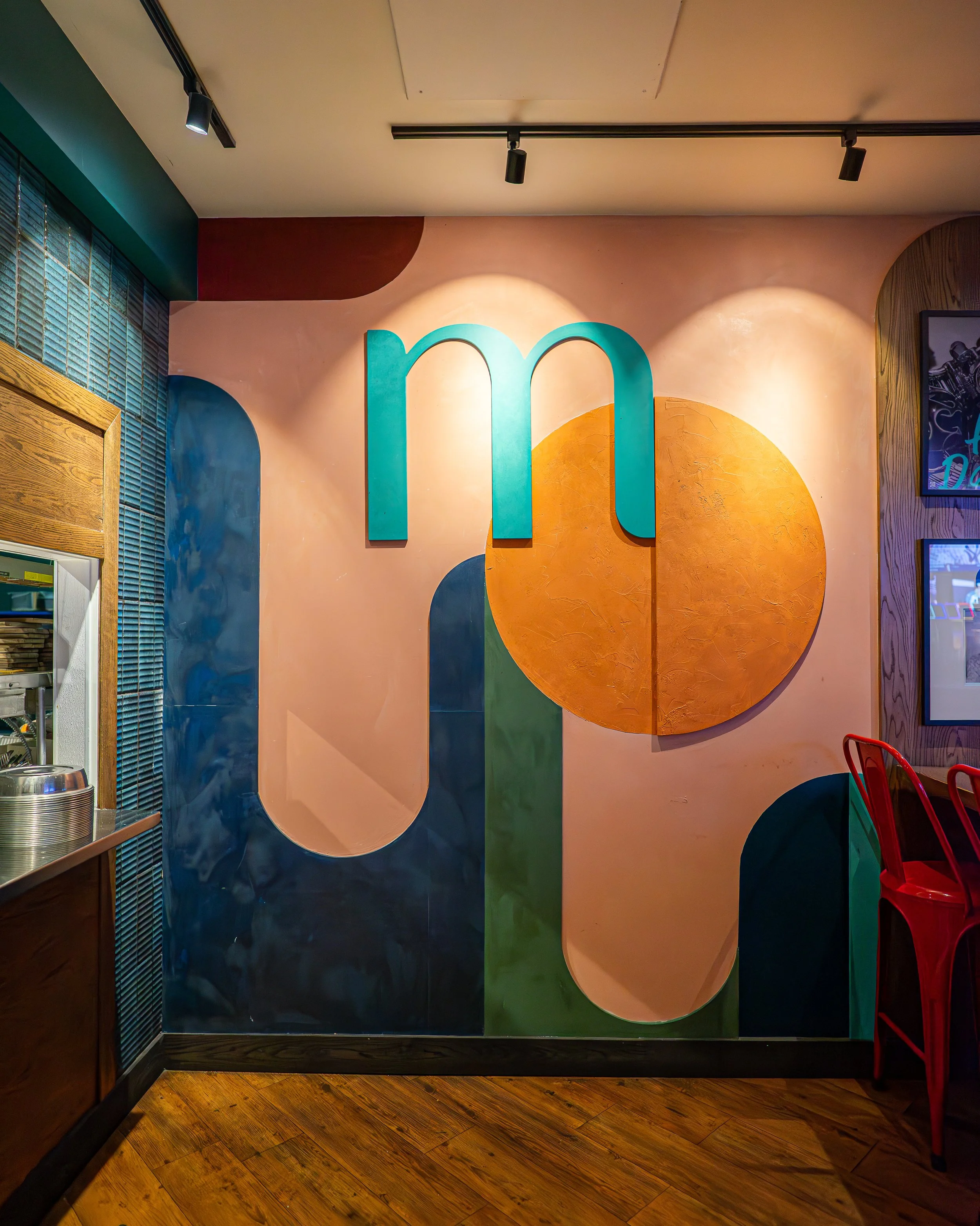 Colorful abstract wall art from Melrose in Calgary AB with geometric shapes and large turquoise letter 'm' in a modern interior.