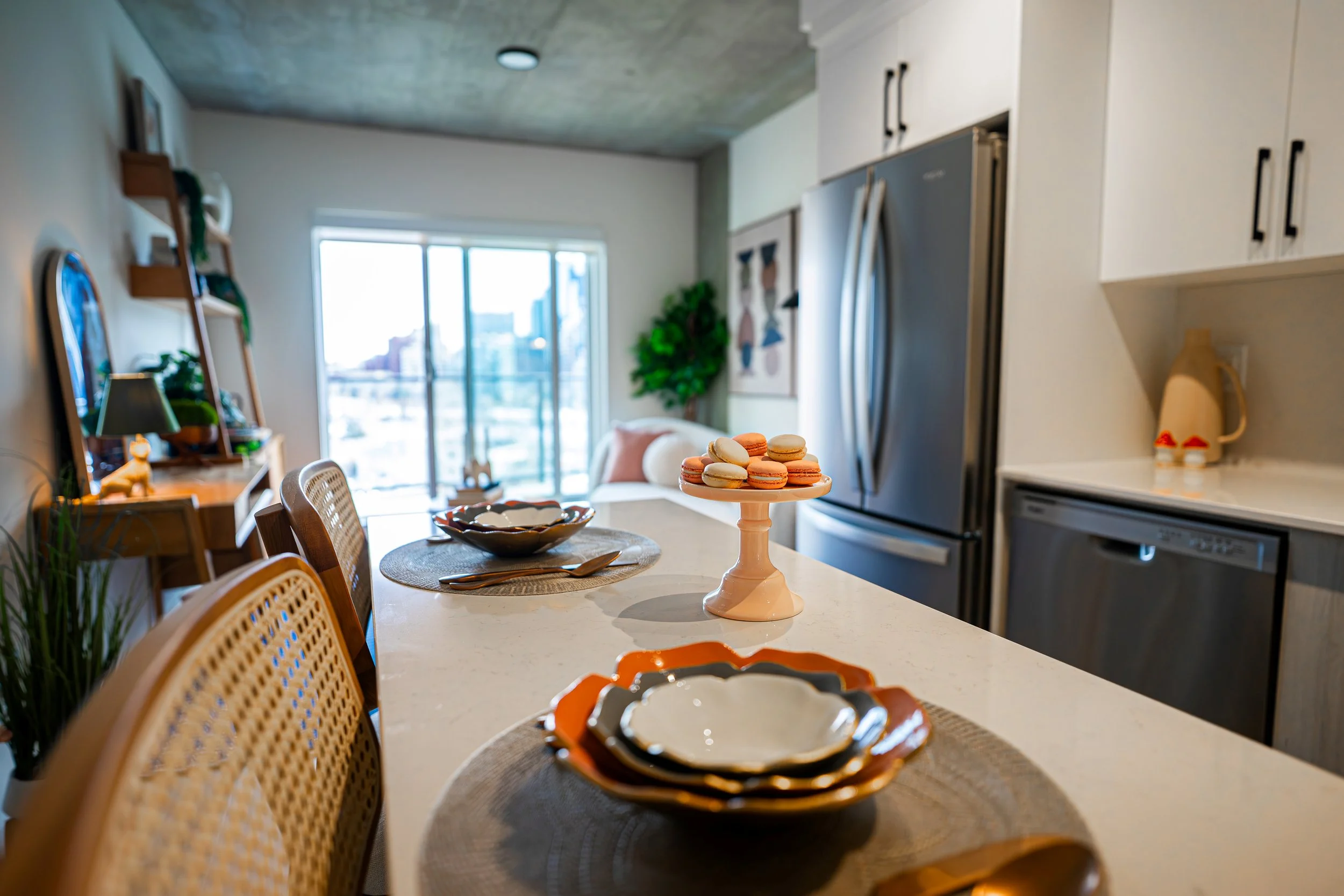 A kitchen with a dining counter set with bowls and a tiered cake stand of macarons, with a living area and large sliding glass doors in the background.