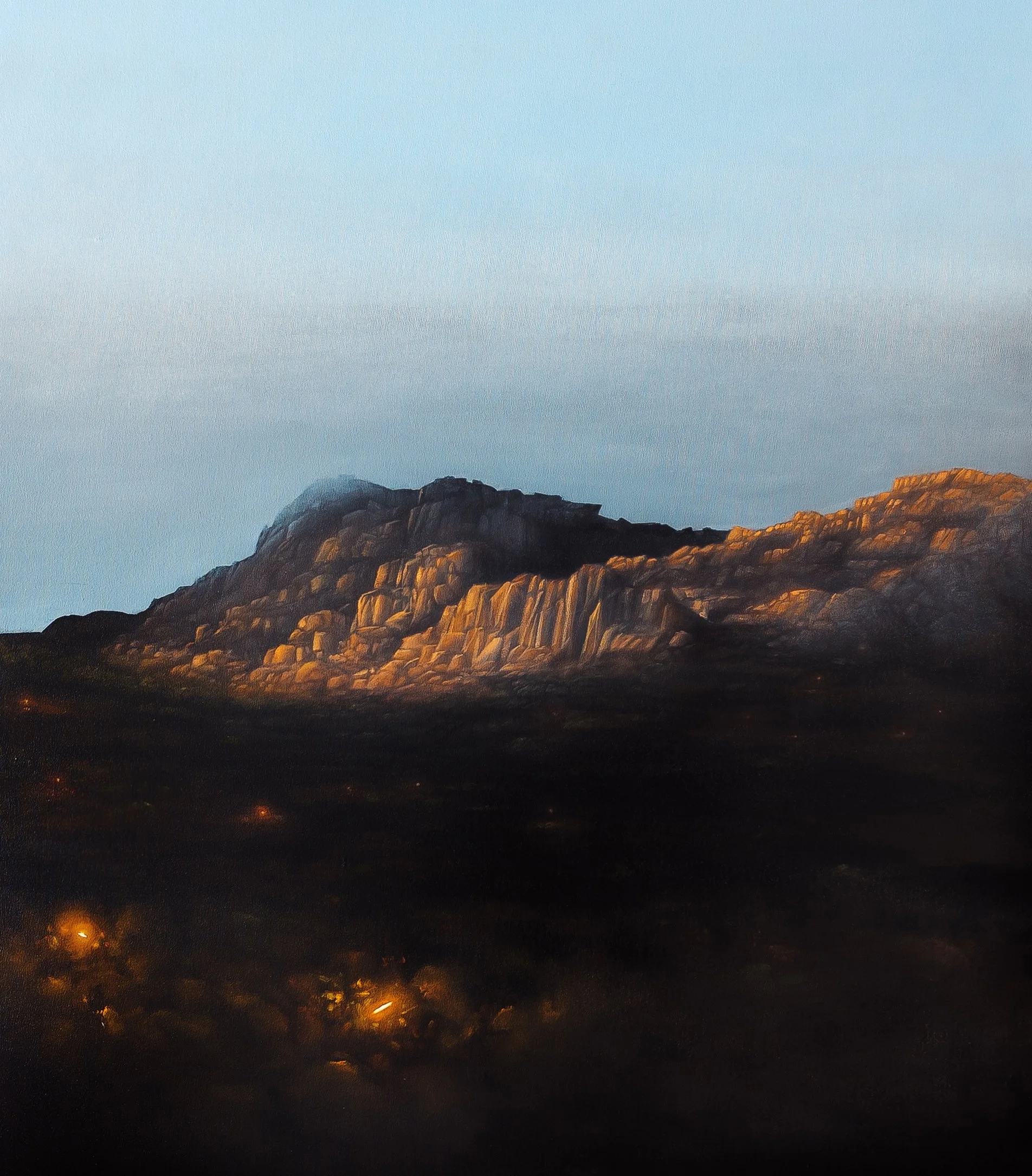 A mountain landscape during sunset with warm orange light illuminating the peaks and a dark foreground.