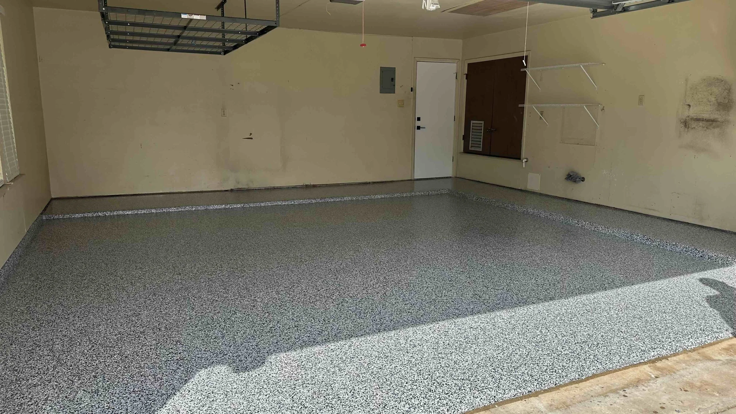 Empty garage with garage door open, concrete floor with epoxy coating, and walls with some stains and marks.
