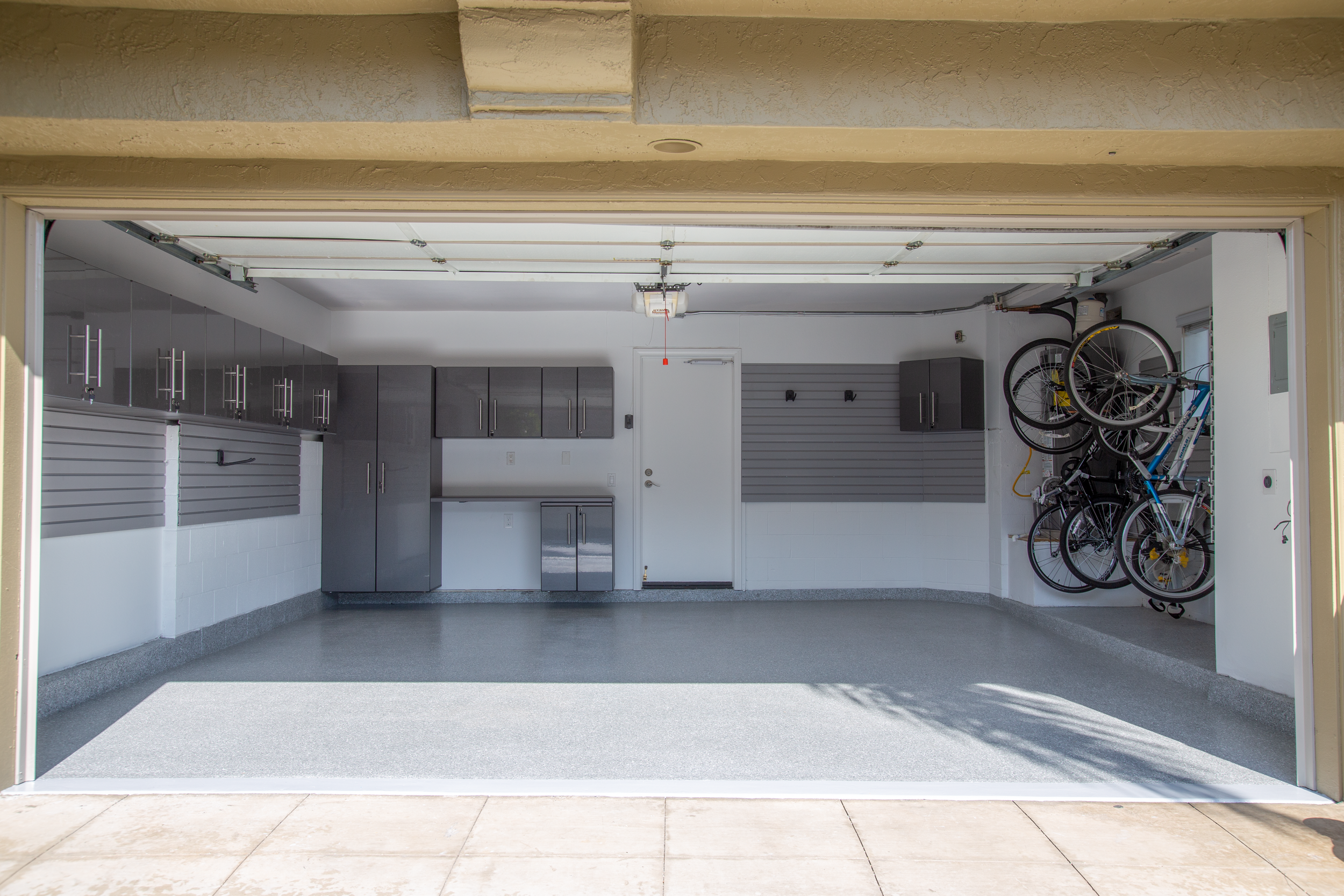 An open garage showing a clean, empty floor, gray cabinets on the left, and bicycles stored on the right side.