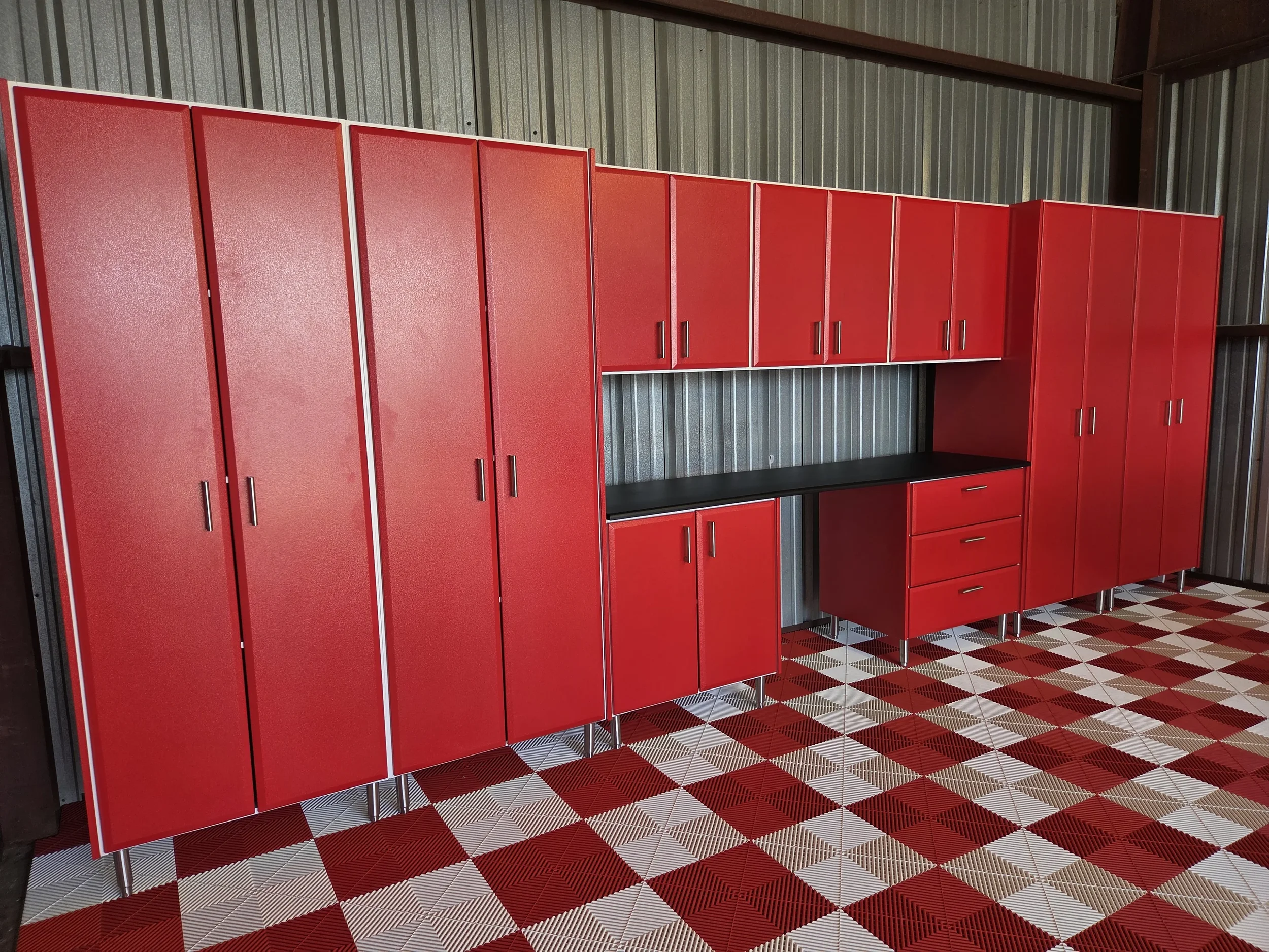 Red lockers with silver handles arranged in a row against a metallic wall inside a building with red and white checkered floor tiles.