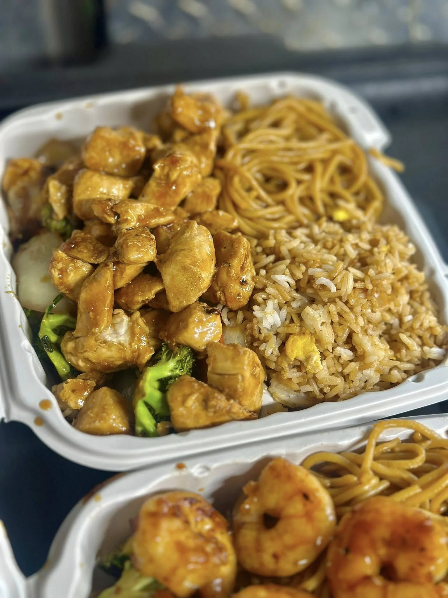 Chinese takeout containers filled with orange chicken, fried rice, lo mein, and vegetable stir-fry.