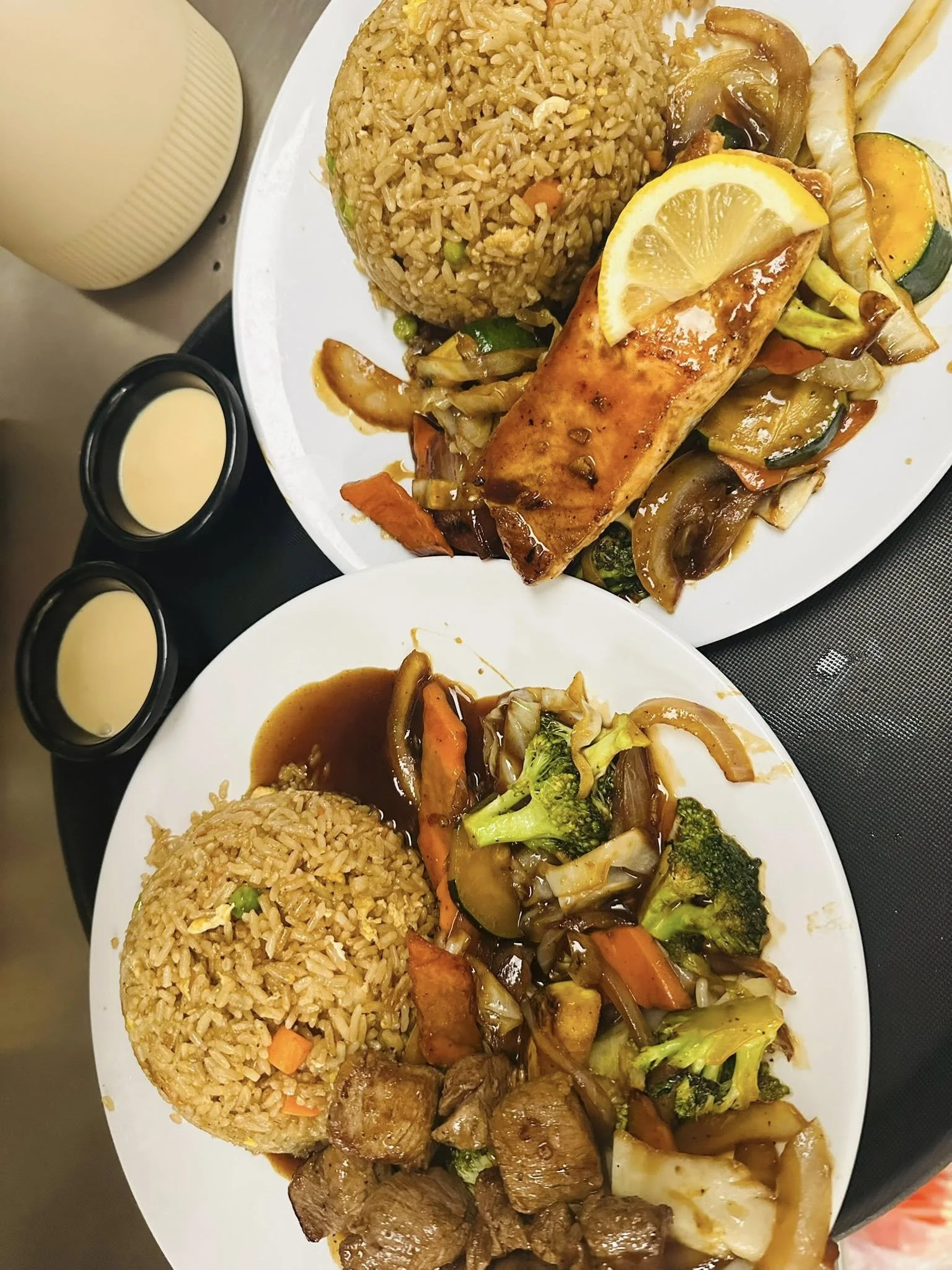 Plate of fried rice, grilled chicken with lemon, stir-fried vegetables including broccoli, carrots, zucchini, cabbage, and onions, with a side of dipping sauces.