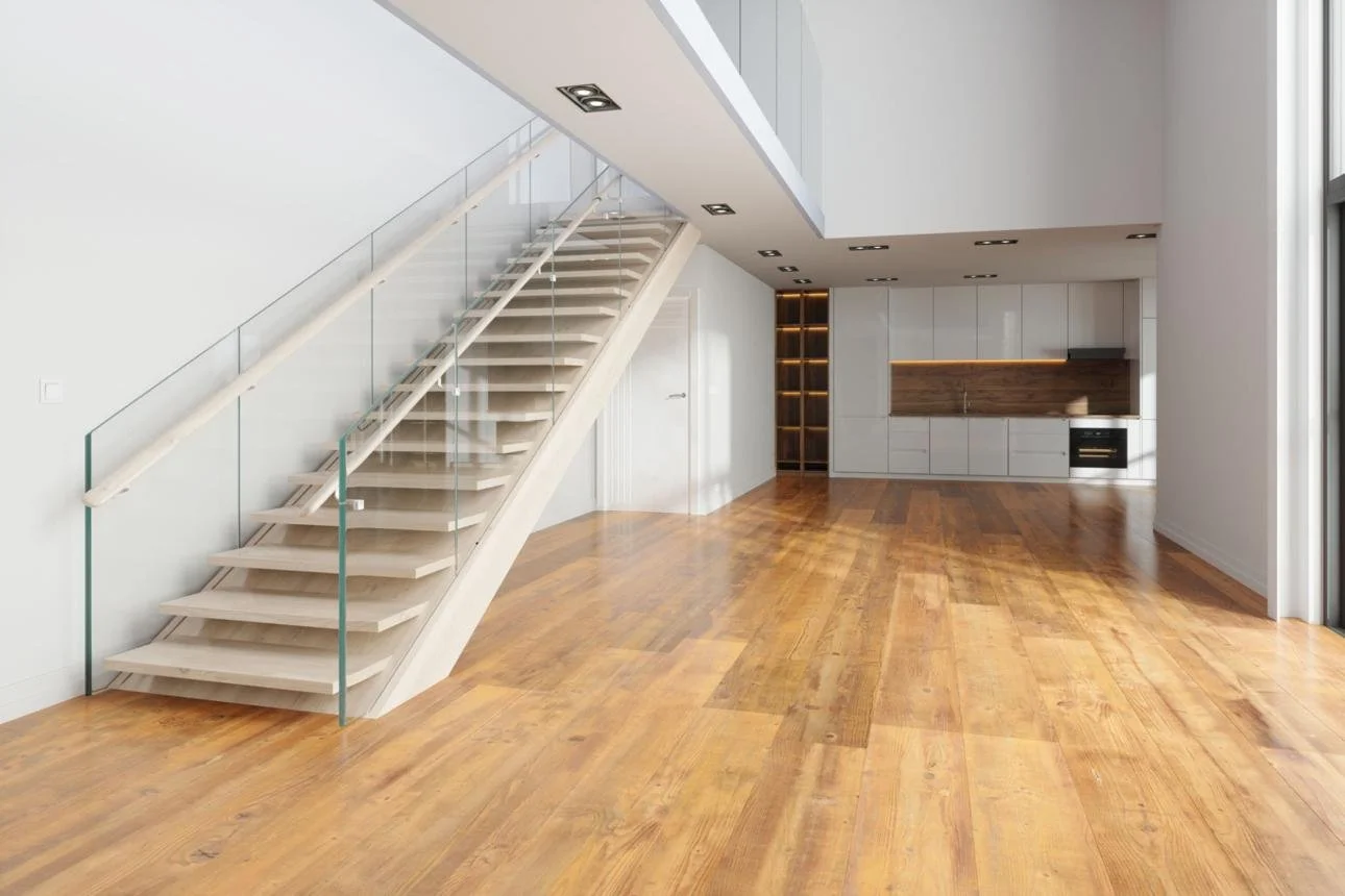 Modern open-concept living space with a staircase leading to an upper floor, featuring wooden flooring, white walls, built-in kitchen cabinetry with wooden accents, and large windows.