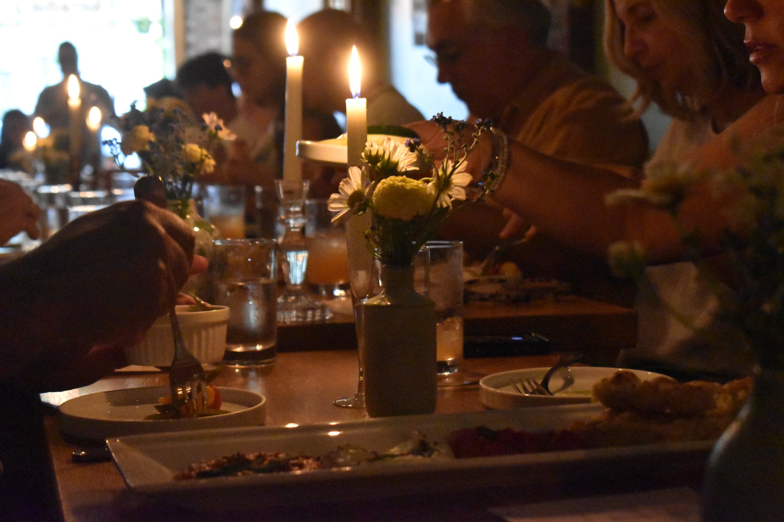 People gathered at a dinner table in a dimly lit restaurant, illuminated by candles and soft lighting, enjoying a meal and conversation.