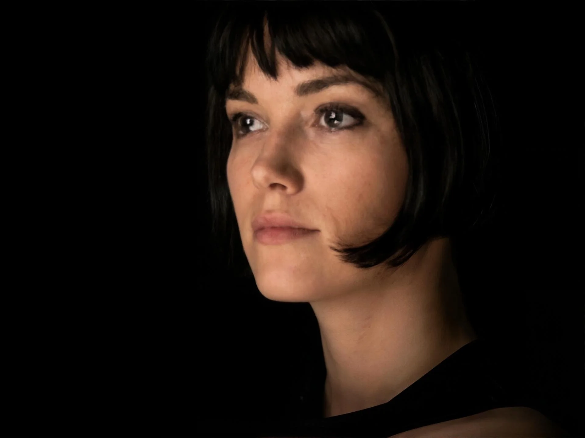 Close-up of a woman's face with short black hair and makeup, against a black background