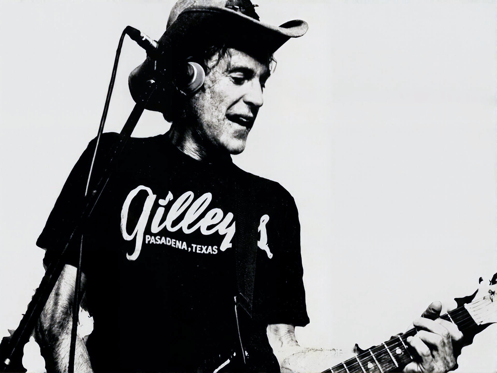 Black and white photograph of a young man wearing a cowboy hat, listening to headphones, and playing an electric guitar.