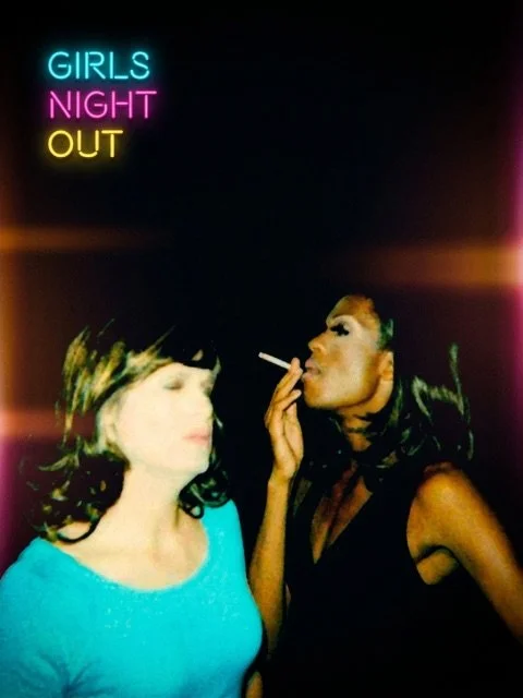 Two women at a nightclub with a neon sign reading 'Girls Night Out'; one woman has curly hair and is wearing a bright blue top, while the other has short hair and is wearing a black outfit and is smoking a cigarette.