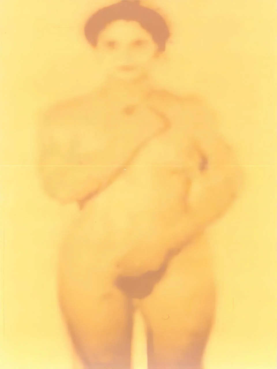 Blurred image of a woman posing with one hand on her hip against a yellow background.