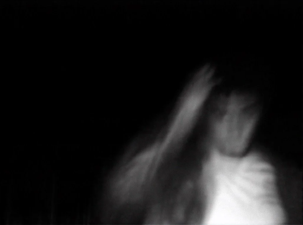 A blurred black-and-white photo of a person with long hair, looking down, possibly in motion.