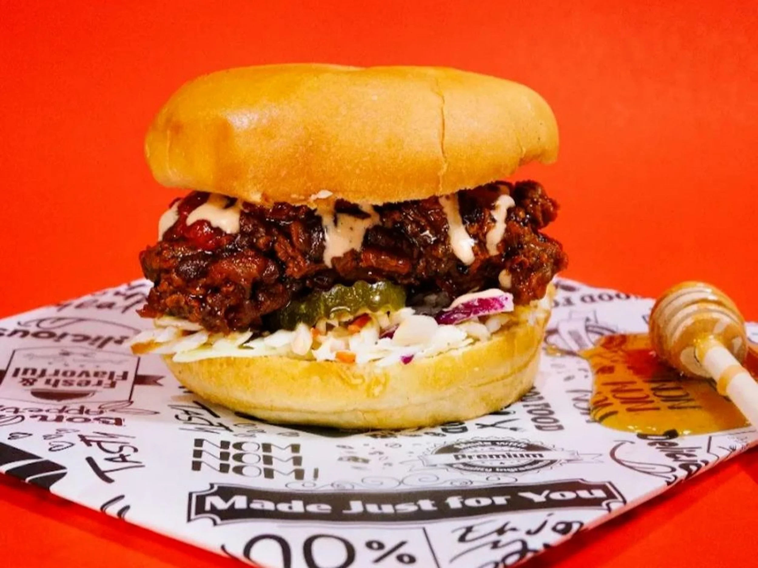 Close-up of a burger with a beef patty, pickles, lettuce, mayonnaise, and a sandwich bun on a colorful, advertising paper-lined tray.