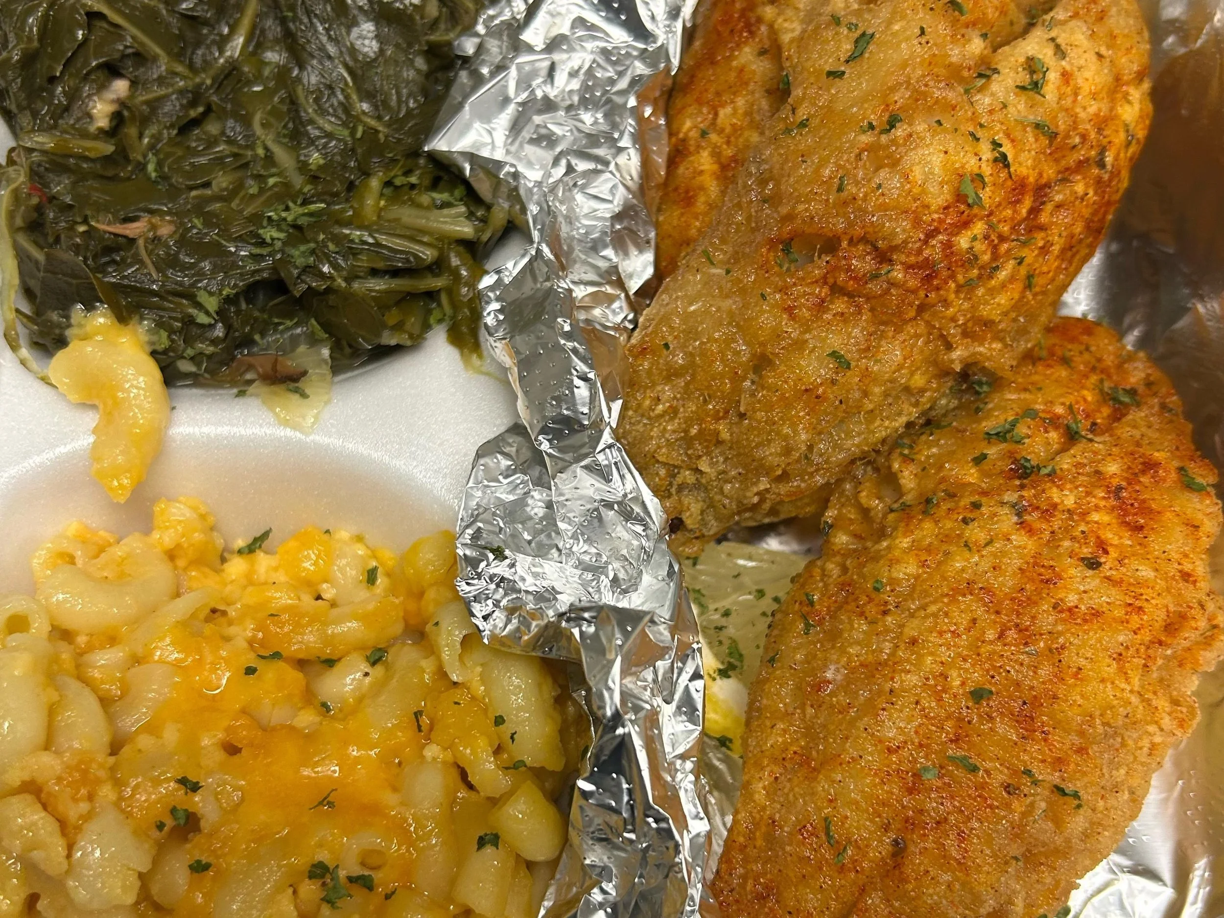Close-up of a meal with two sides: on the left, creamed macaroni and cheese with melted cheese and chopped herbs, on the right, breaded fried fish fillets sprinkled with parsley, served on aluminum foil.