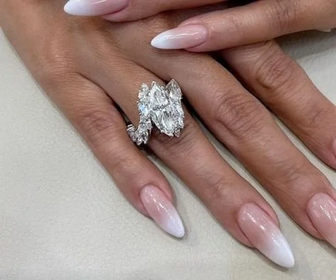 Close-up of a hand with long, manicured nails holding a large, shiny diamond ring.