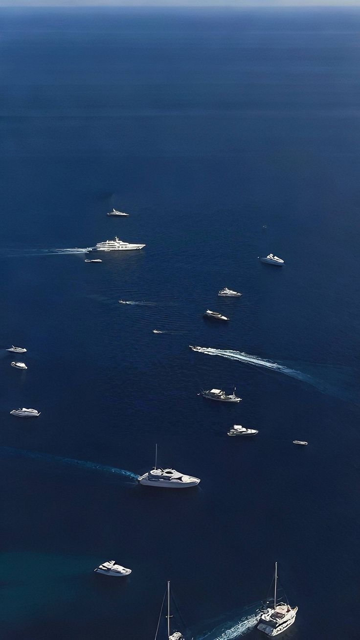 Multiple yachts and boats sailing in a large, open ocean with deep blue water