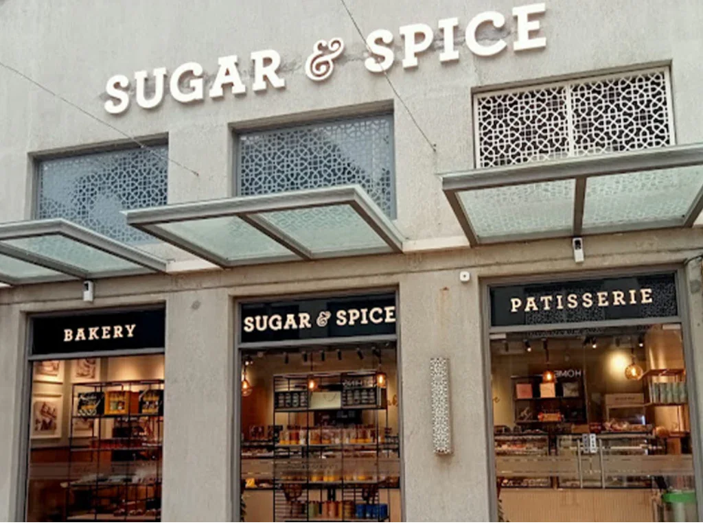 Storefront of Sugar & Spice bakery, patisserie, and sugar shop with large windows and black signs.