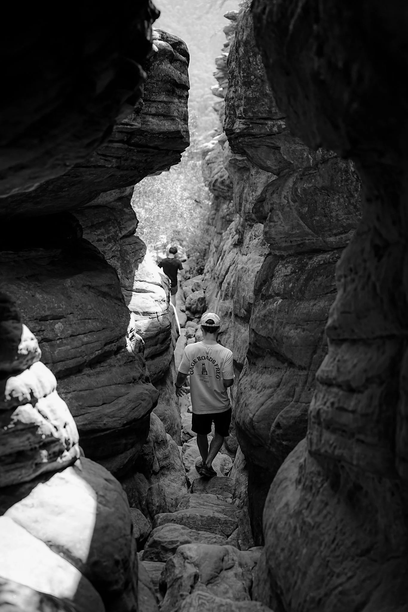 People hiking through a narrow, rocky canyon with towering rock walls on either side.