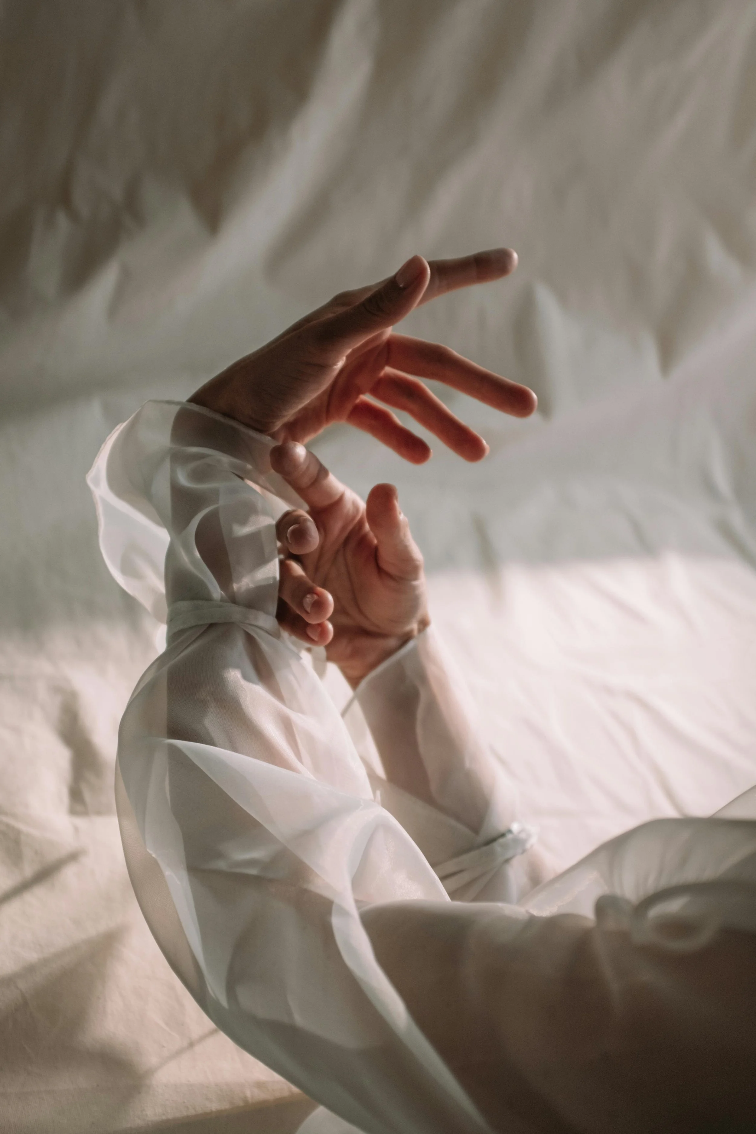 Close-up of a person's hand with long fingers, wearing a white blouse with puffy sleeves, reaching upward against a textured beige background.