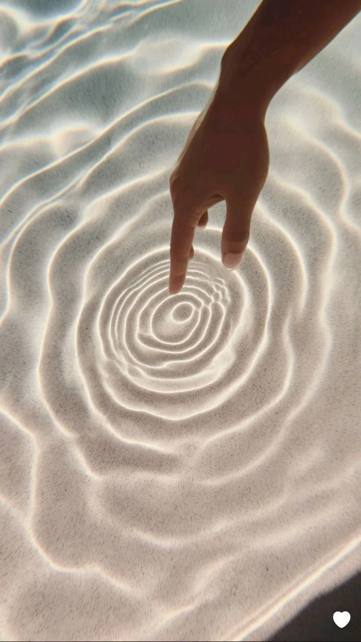 A person's hand with a finger pointing towards ripples on the surface of clear water.