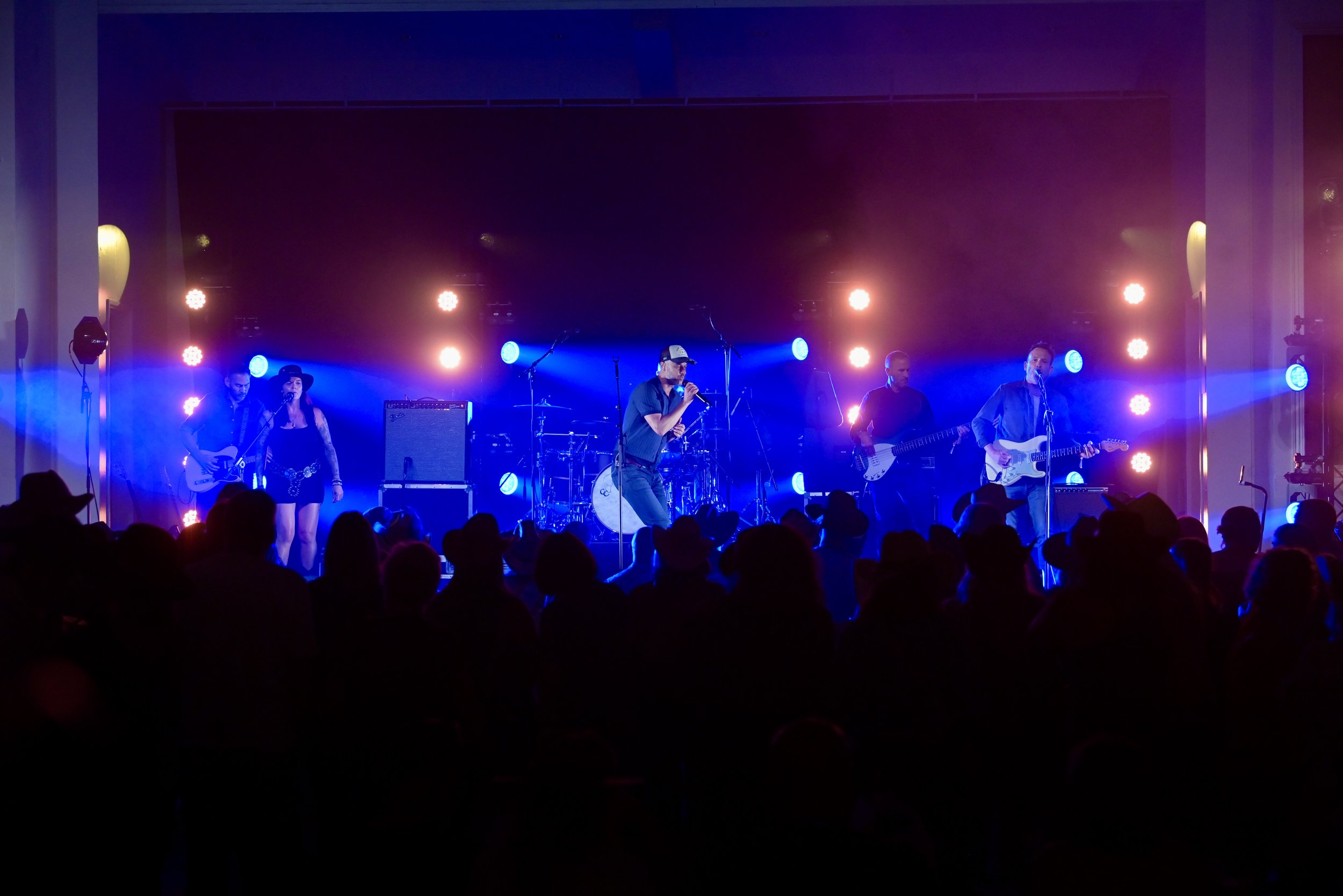 The Jackson Line performing live on stage with colourful lighting, including blue and purple hues, and silhouettes of audience members watching. Photo by Dave Nelson at The British Country Music Festival.