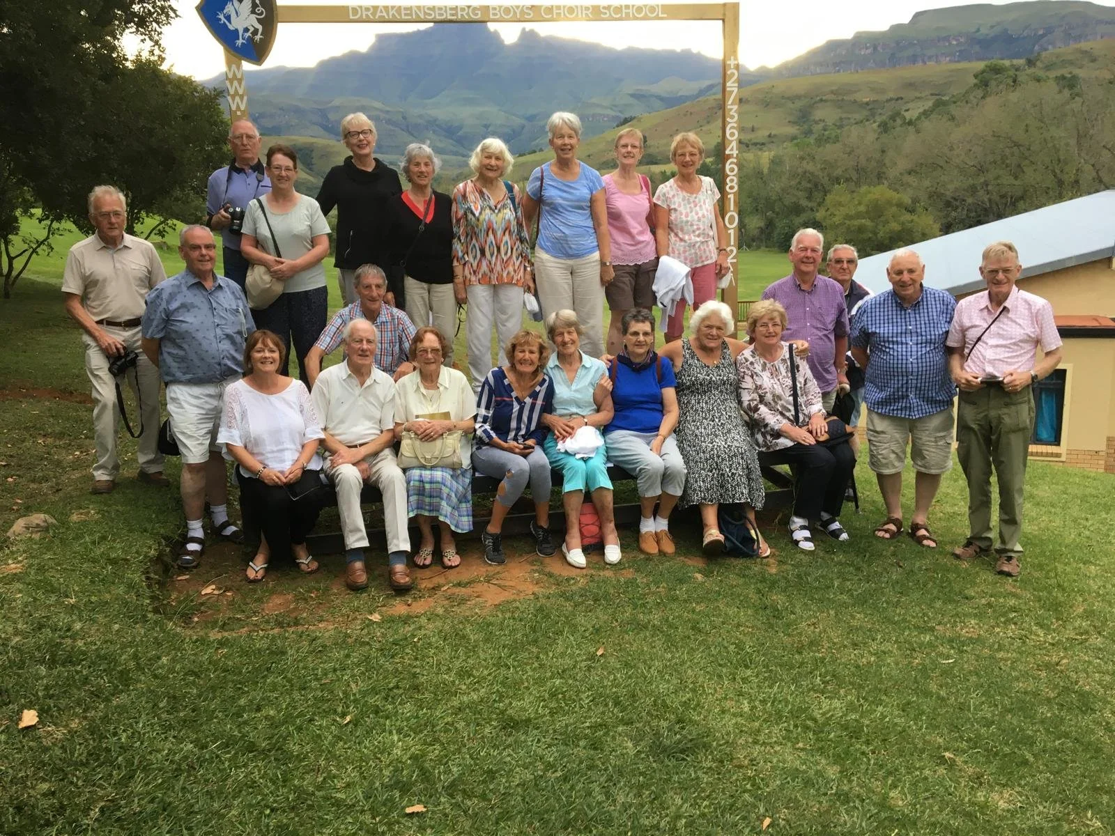 Group of seniors posing outdoors in front of a frame that reads "Drakensberg Boys Choir School" with a mountainous landscape in the background.