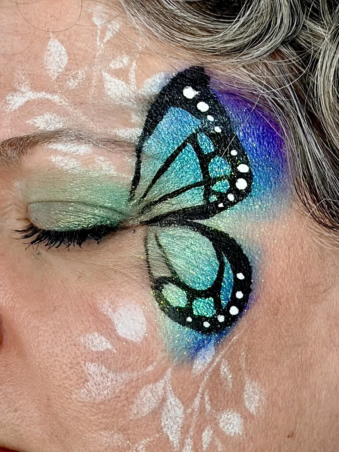 Nahaufnahme eines Auges mit buntem Schmetterlingslinsen-Make-up, grünen Lidschatten und weißen Akzenten.