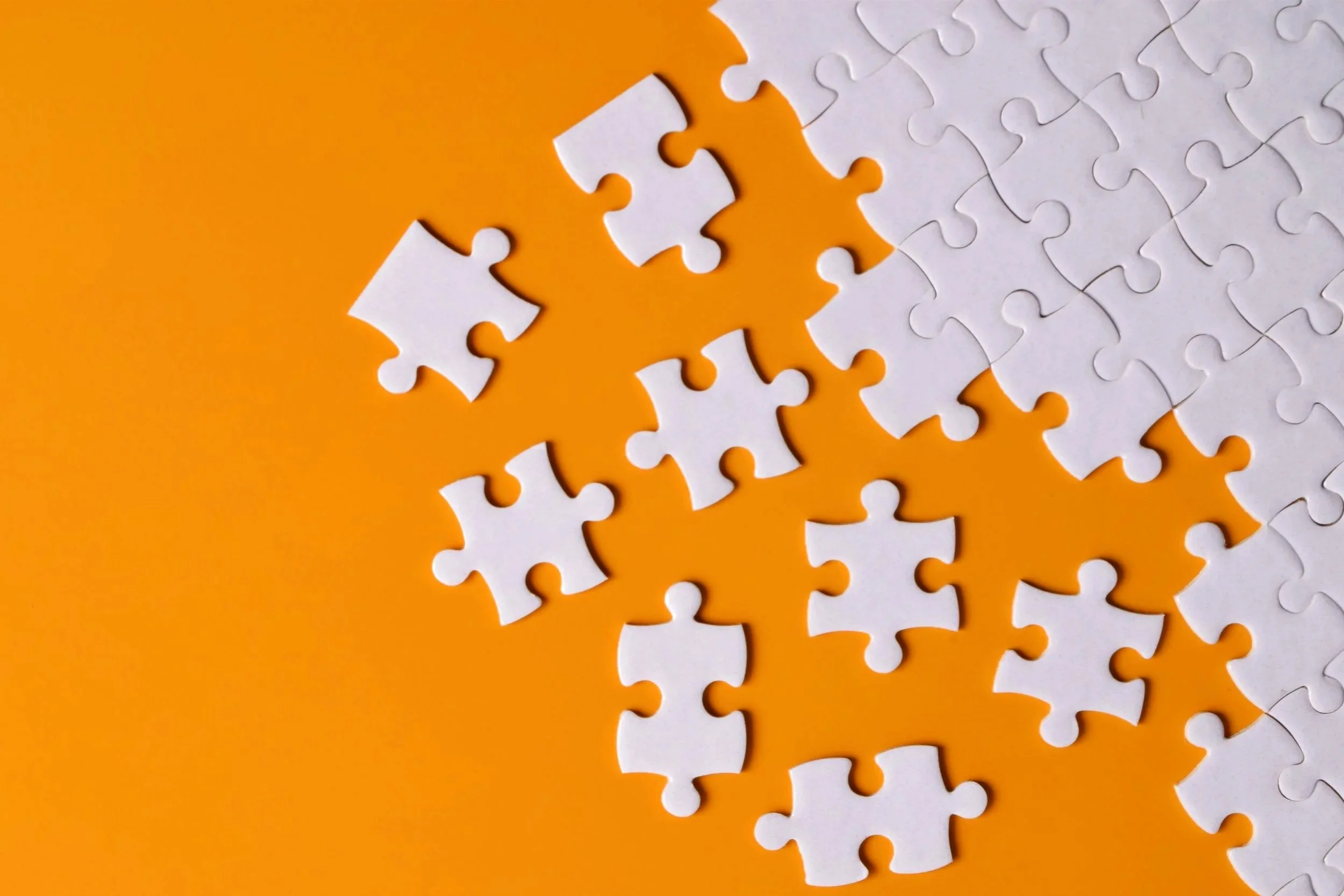 Close-up of a partially assembled white jigsaw puzzle on an orange background, with several pieces missing.