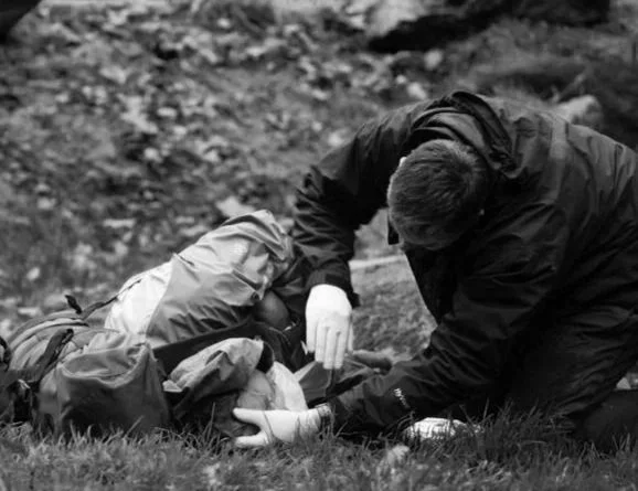 A person performing first aid on another person lying on the ground in an outdoor setting.