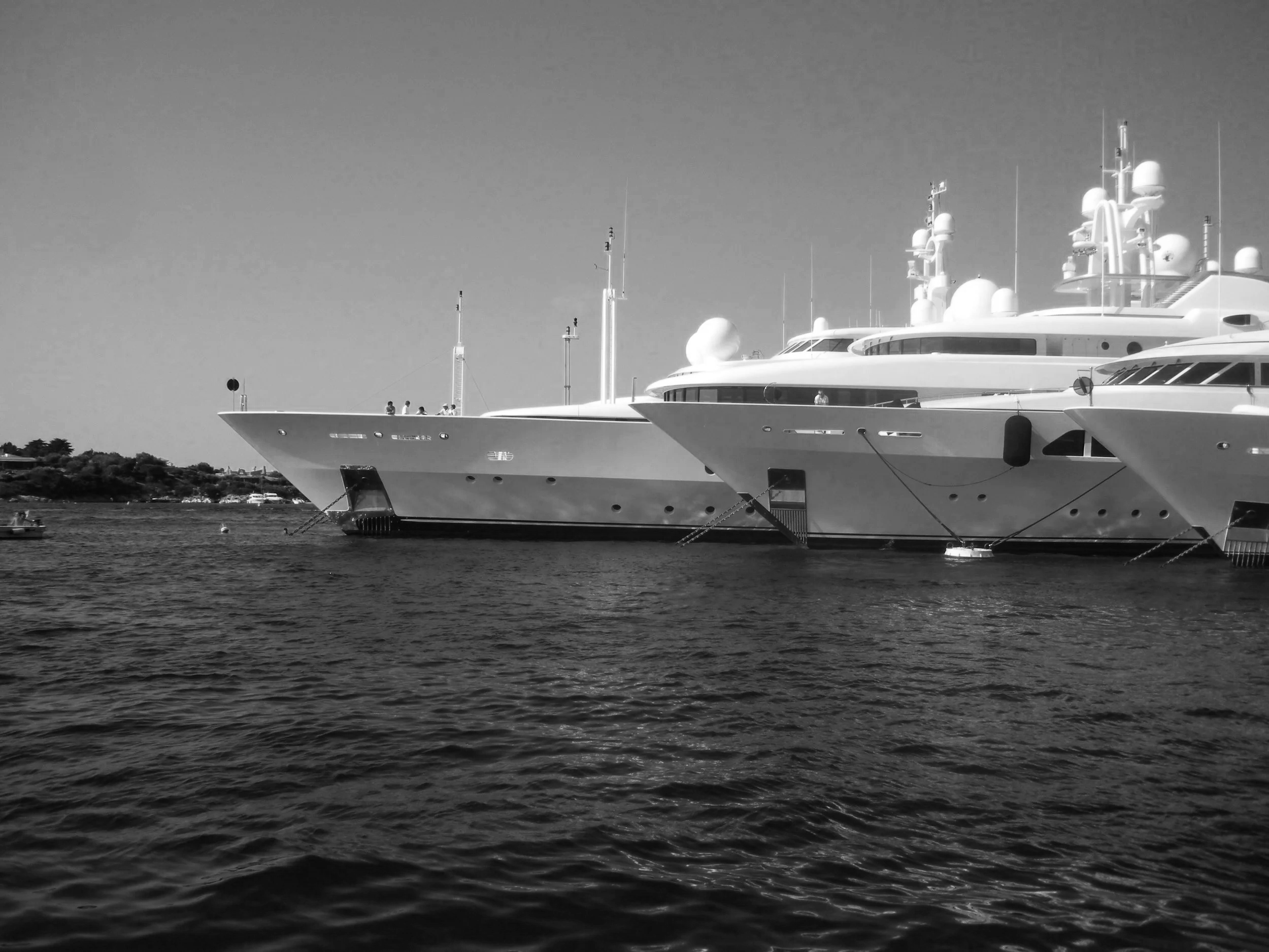 A large luxury yacht docked in a harbor, with several antennas and satellite dishes on top, and small boats floating nearby.
