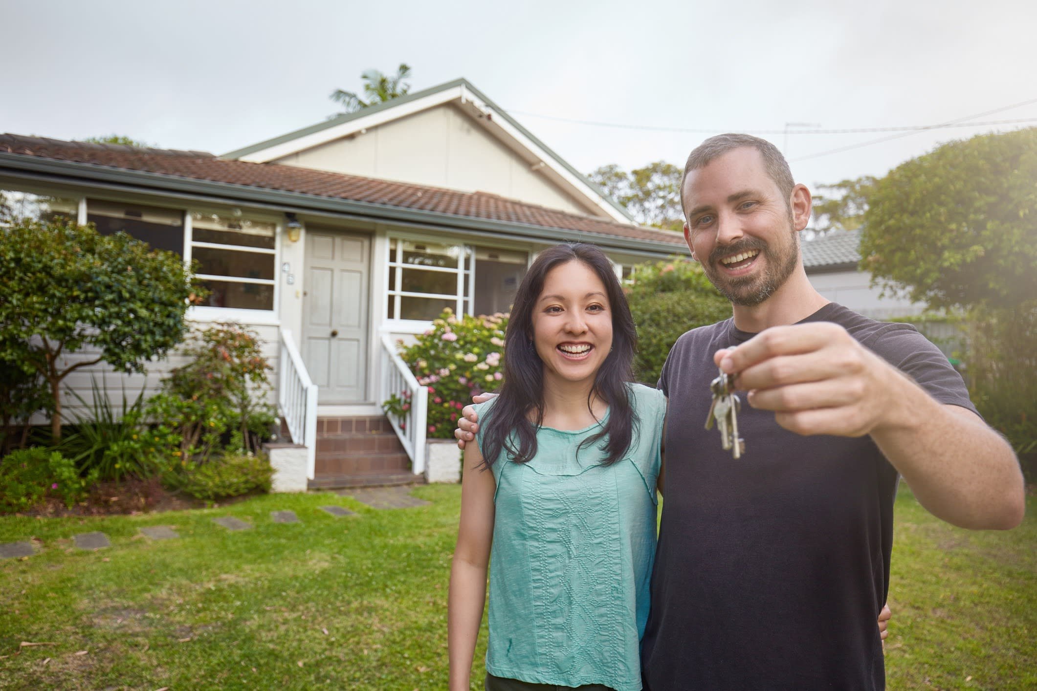 A man and a young girl smiling and taking a selfie in front of a house with a garden.