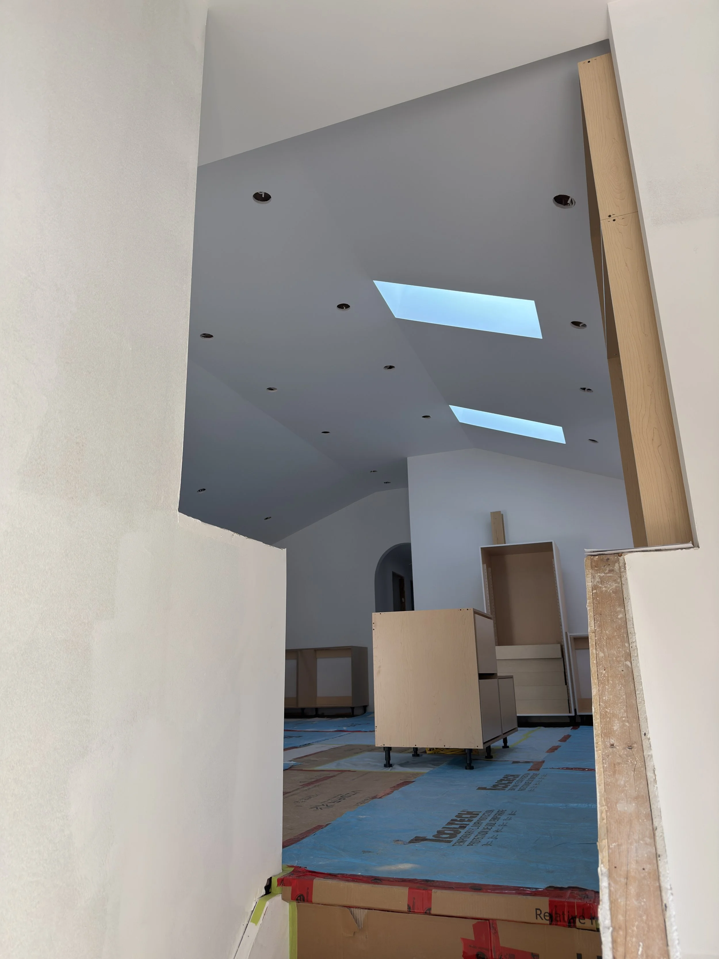 Interior of a living room in Etobicoke under construction with walls primed after drywall and taping installation, ceiling with recessed lighting holes, skylights present.