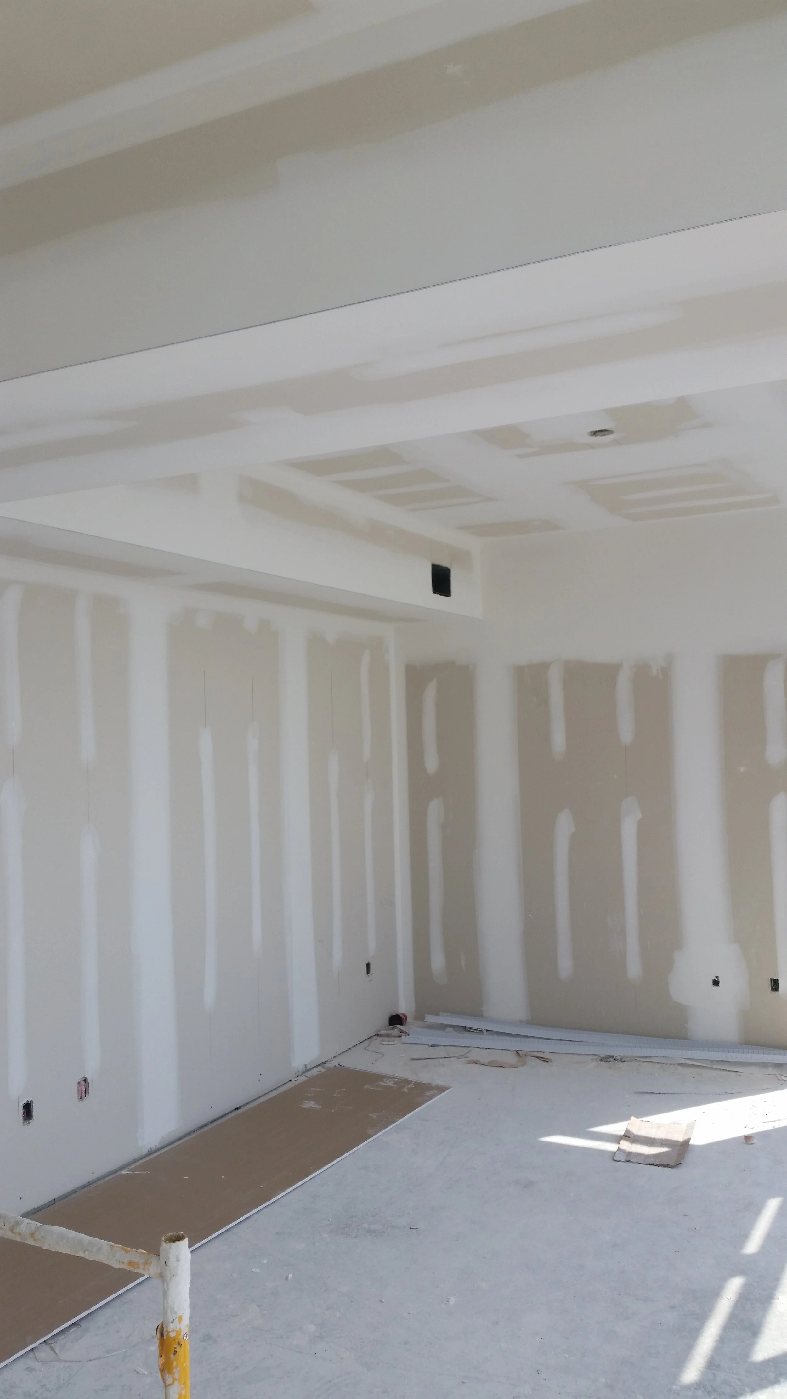 Interior of a room under construction with drywall walls and ceiling in Toronto, and a window letting in sunlight.