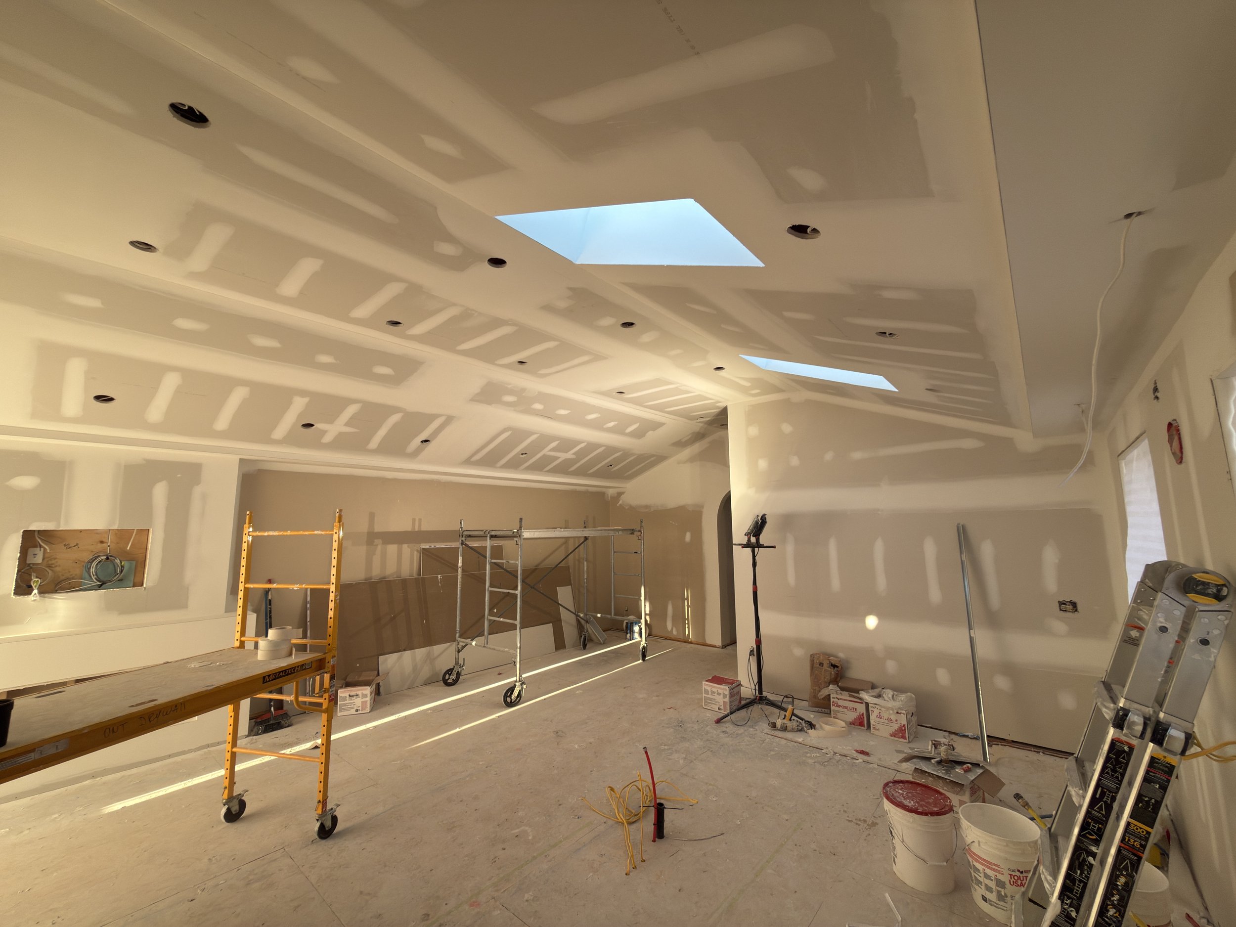 Interior room under construction with drywall, scaffolding, ladders, tools, and a ceiling skylight in Toronto.