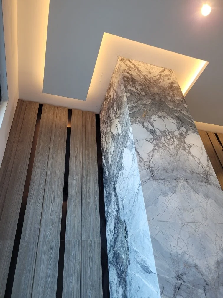 Interior ceiling with modern recessed lighting, a large marble pillar with gray and white veining, and a wall with vertical wooden slats.