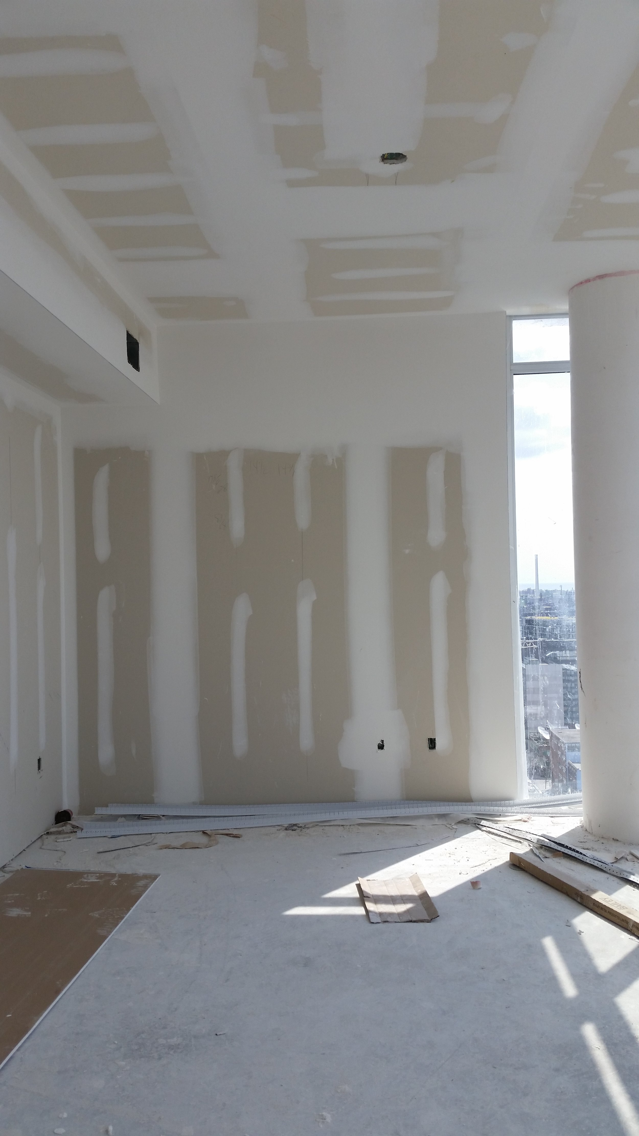Room with drywall installation and patching, with a large window showing a cityscape outside. In Toronto.