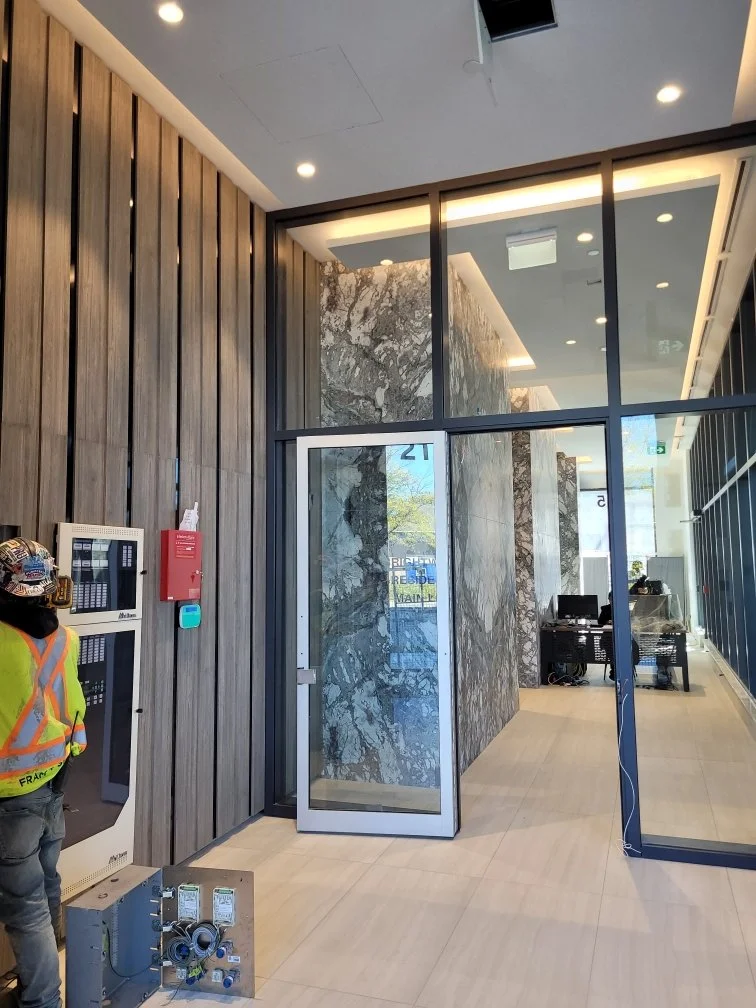 Modern interior office entrance with glass door, marble walls, wood paneling, and a security system