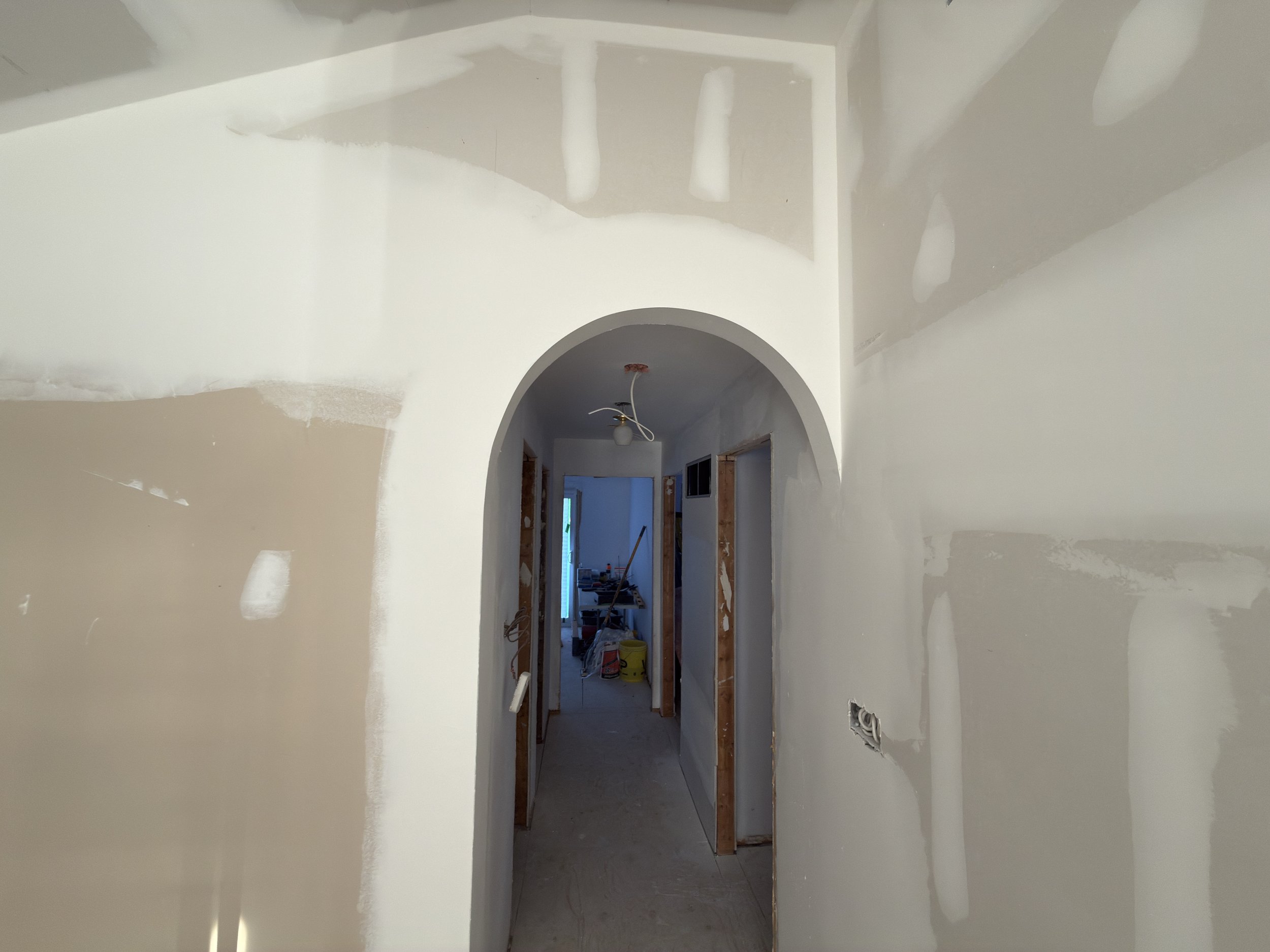 Interior of a house in Toronto under construction, with drywall and unfinished walls. An archway leads into a corridor with quality taping and drywall installed.