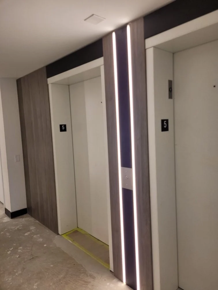Two elevator doors in a modern building, with the left one open, showing a floor indicator reading 5, and decorative lighting featuring vertical lines on the right side.