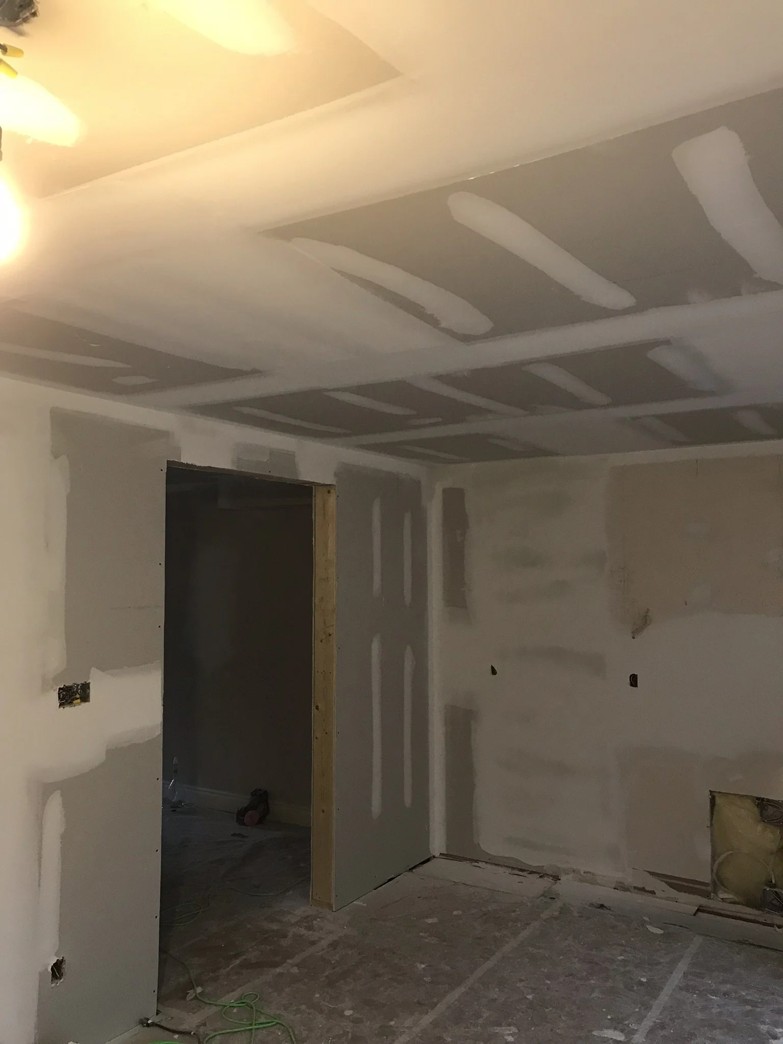Interior room in the process of being renovated with drywall installation, electrical outlets, and a partially built wall.