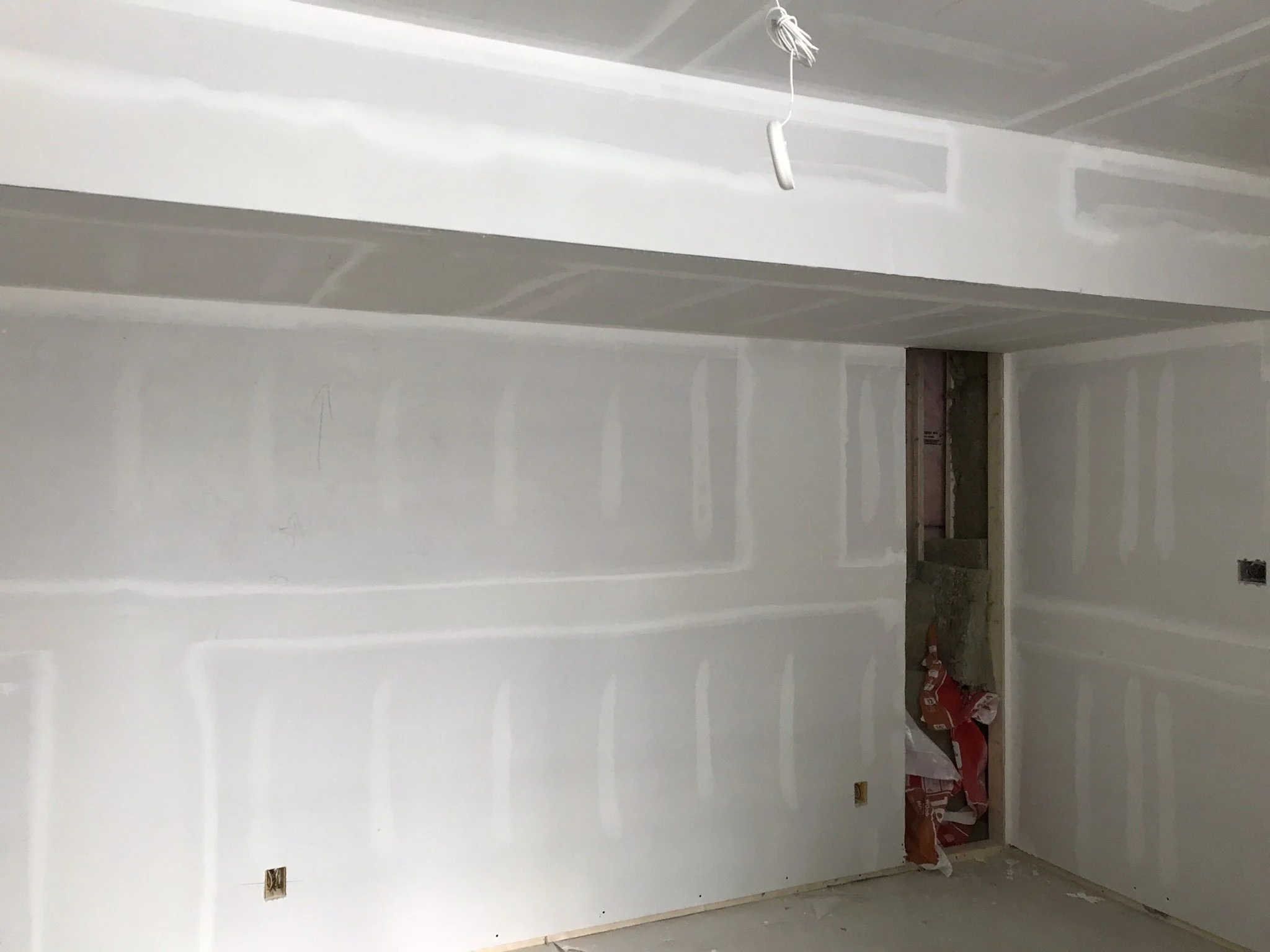 Interior of a room under construction, with white drywall installed on the walls and ceiling, in Oakville.