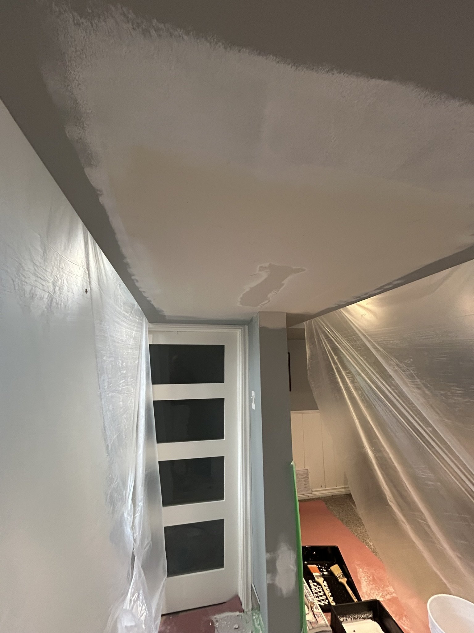 A room under renovation with a partially painted wall, plastic coverings on the floor and furniture, and a window with four panes.