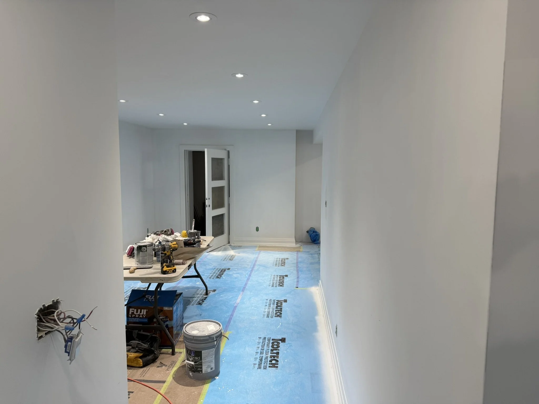 A room under renovation with construction tools, paint supplies, and wiring, with finished walls and ceiling with recessed lighting in Mississauga.