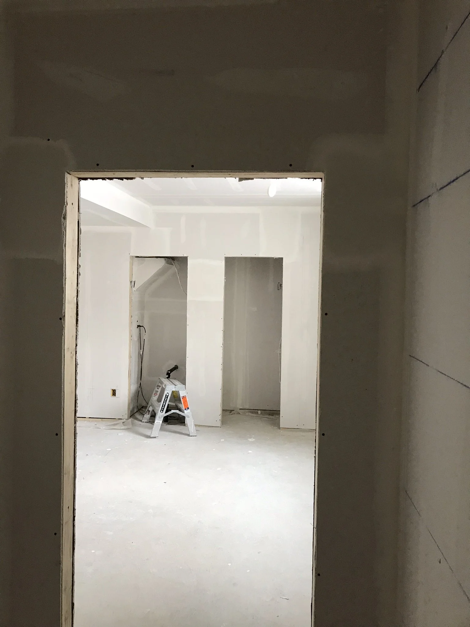Construction site with unfinished white walls, a stepladder, and construction tools in an empty room.