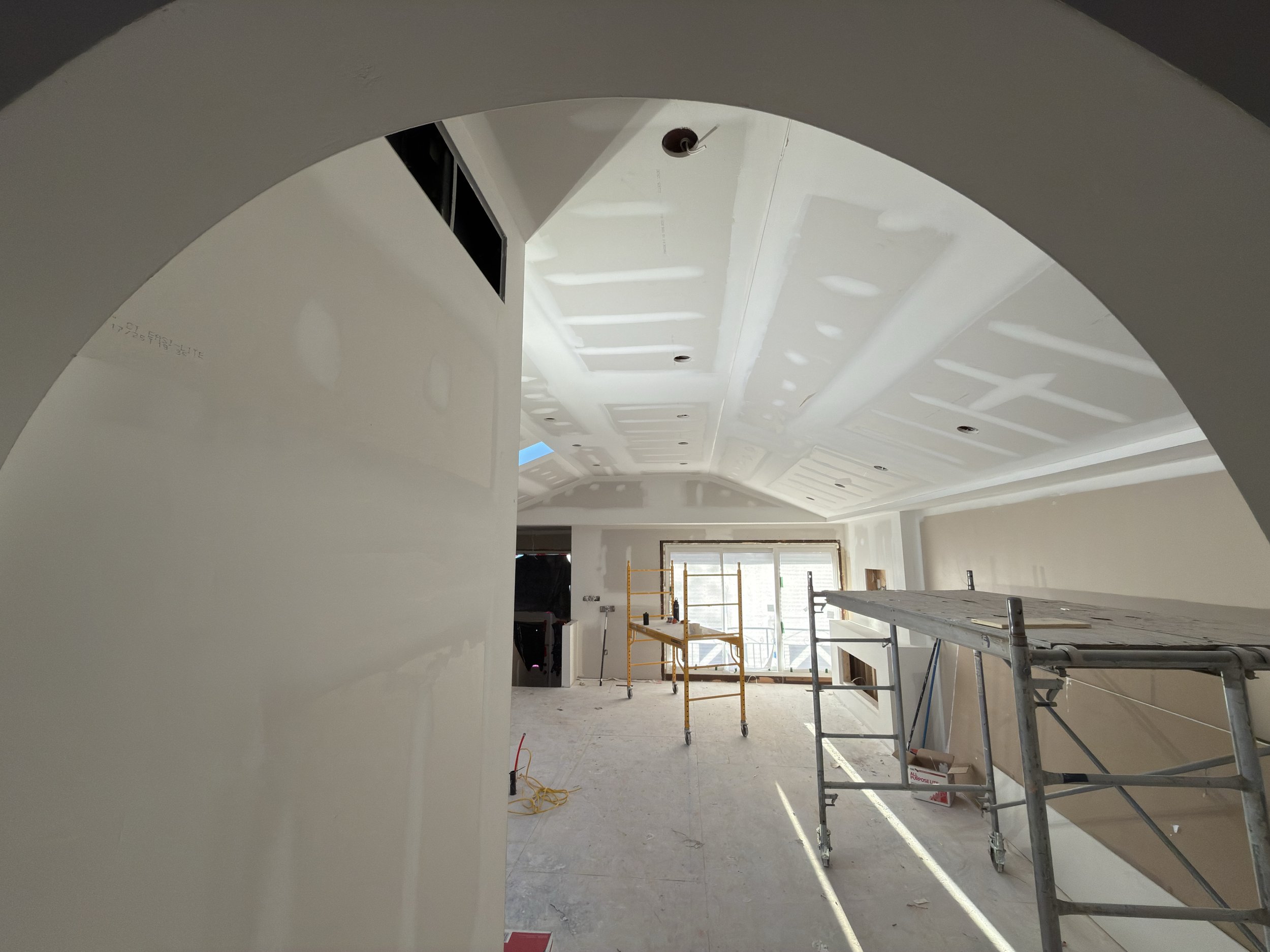 Interior of a house in Mississauga under construction with scaffolding, taped drywall, and ceiling with recessed lighting, viewed through an arched doorway.