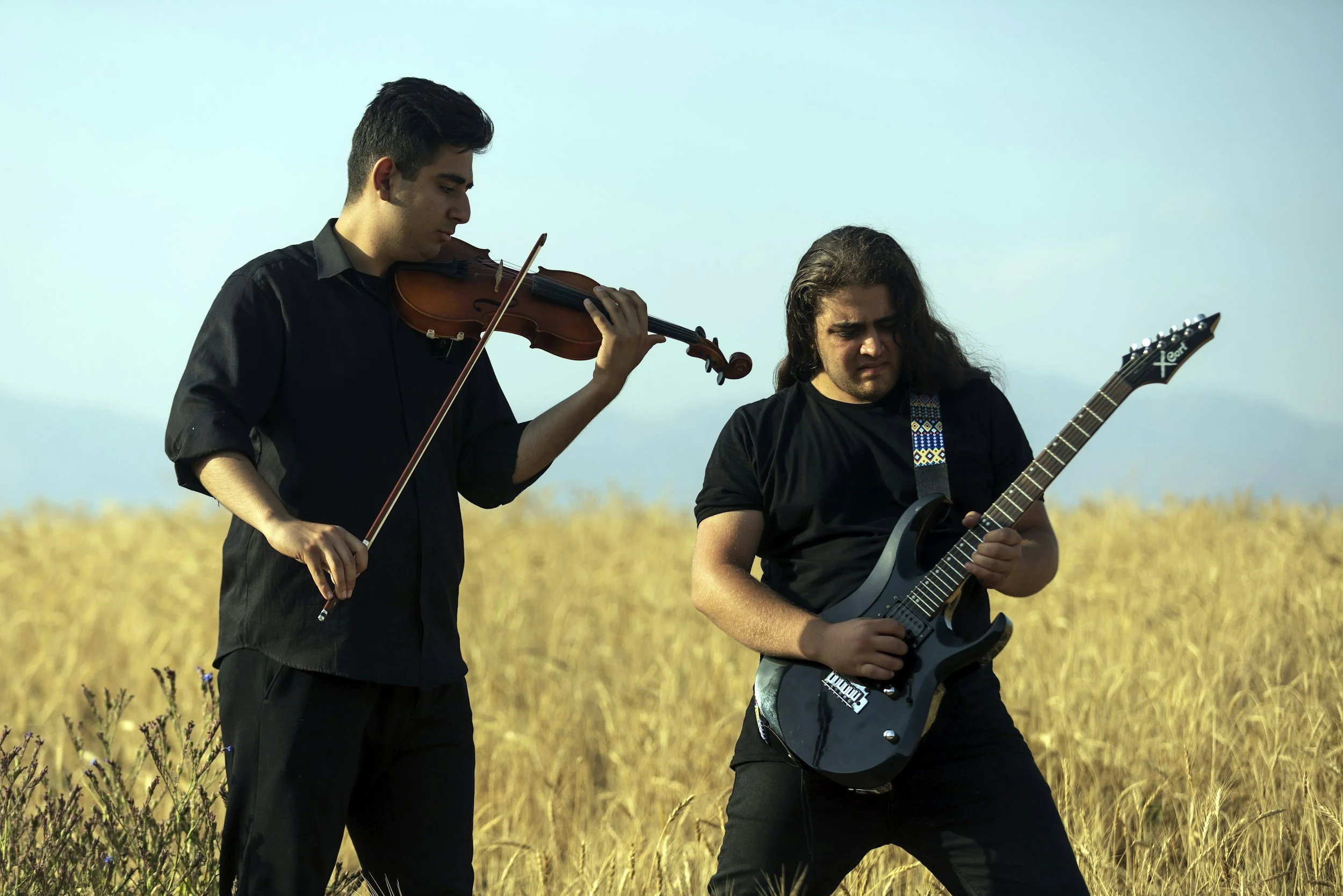 Two musicians playing guitar and violin outdoors in a field under a clear sky.