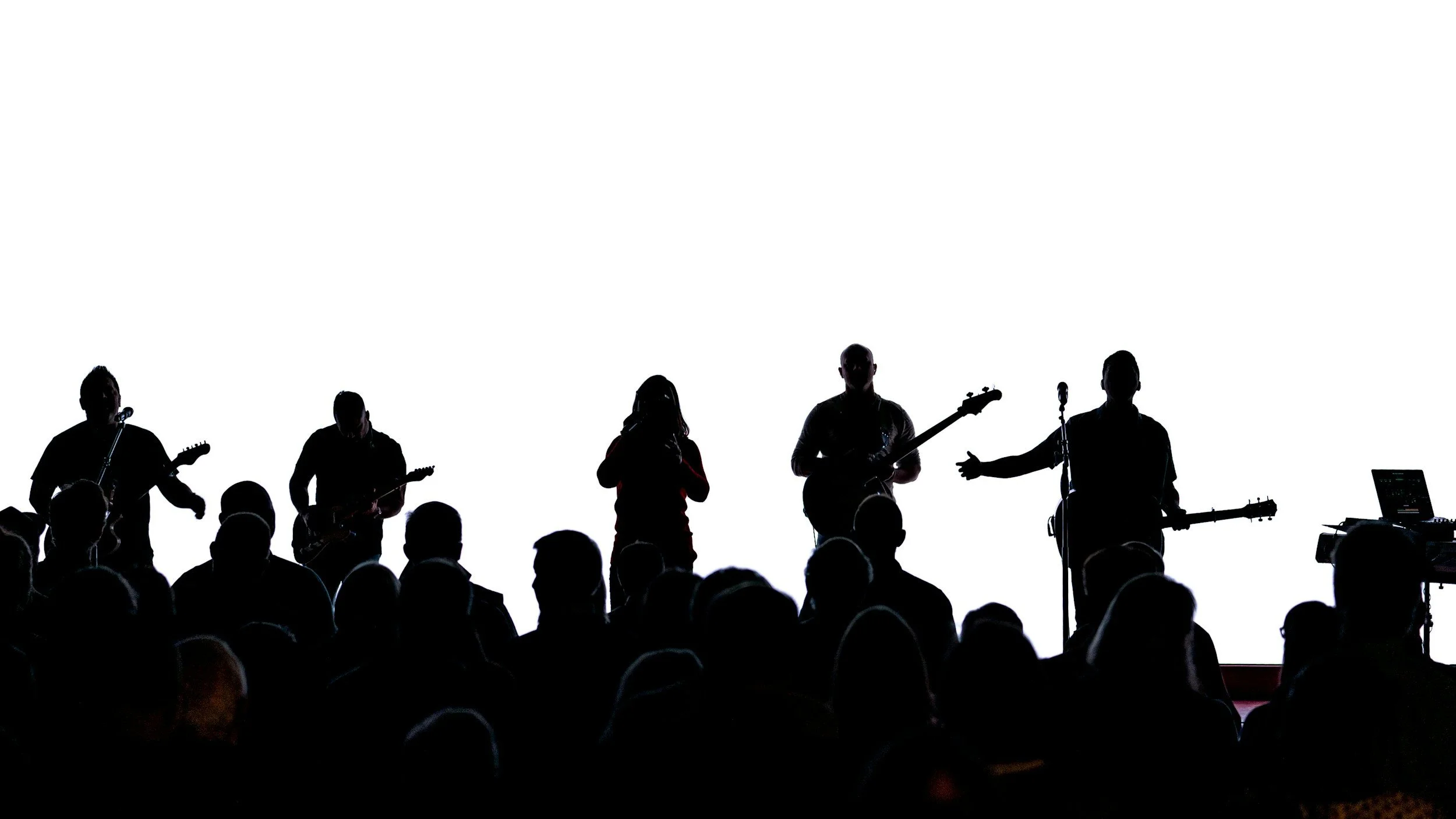 A group of musicians performing on stage with a bright white background, with silhouettes of audience members in the foreground.