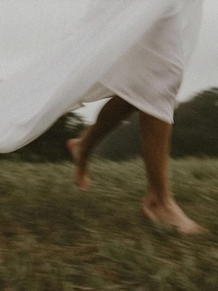 Person walking barefoot on grass, wearing white pants and a white top.
