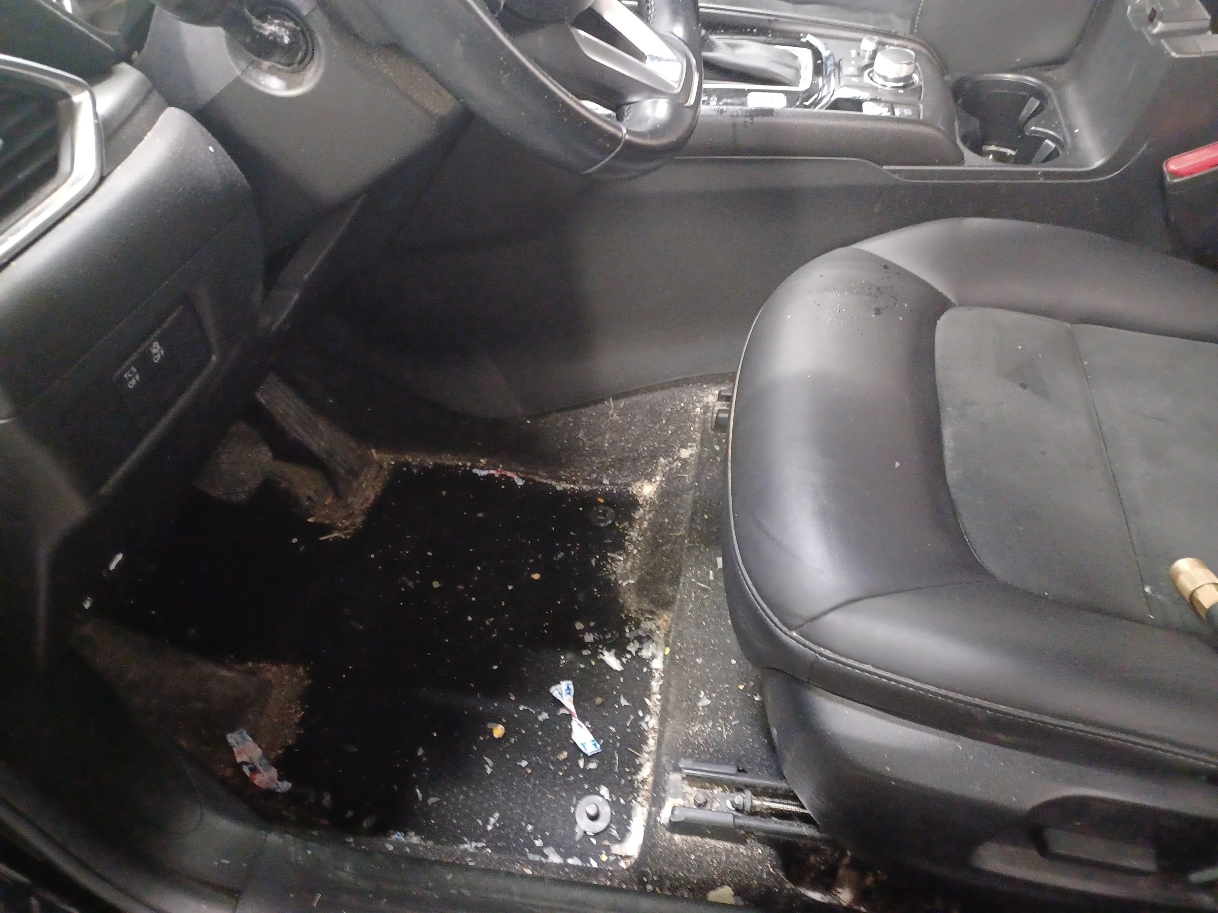 A car interior shows the front passenger seat and center console, with the glove compartment open revealing a missing or damaged air vent and scattered debris and dirt on the floor and seat.