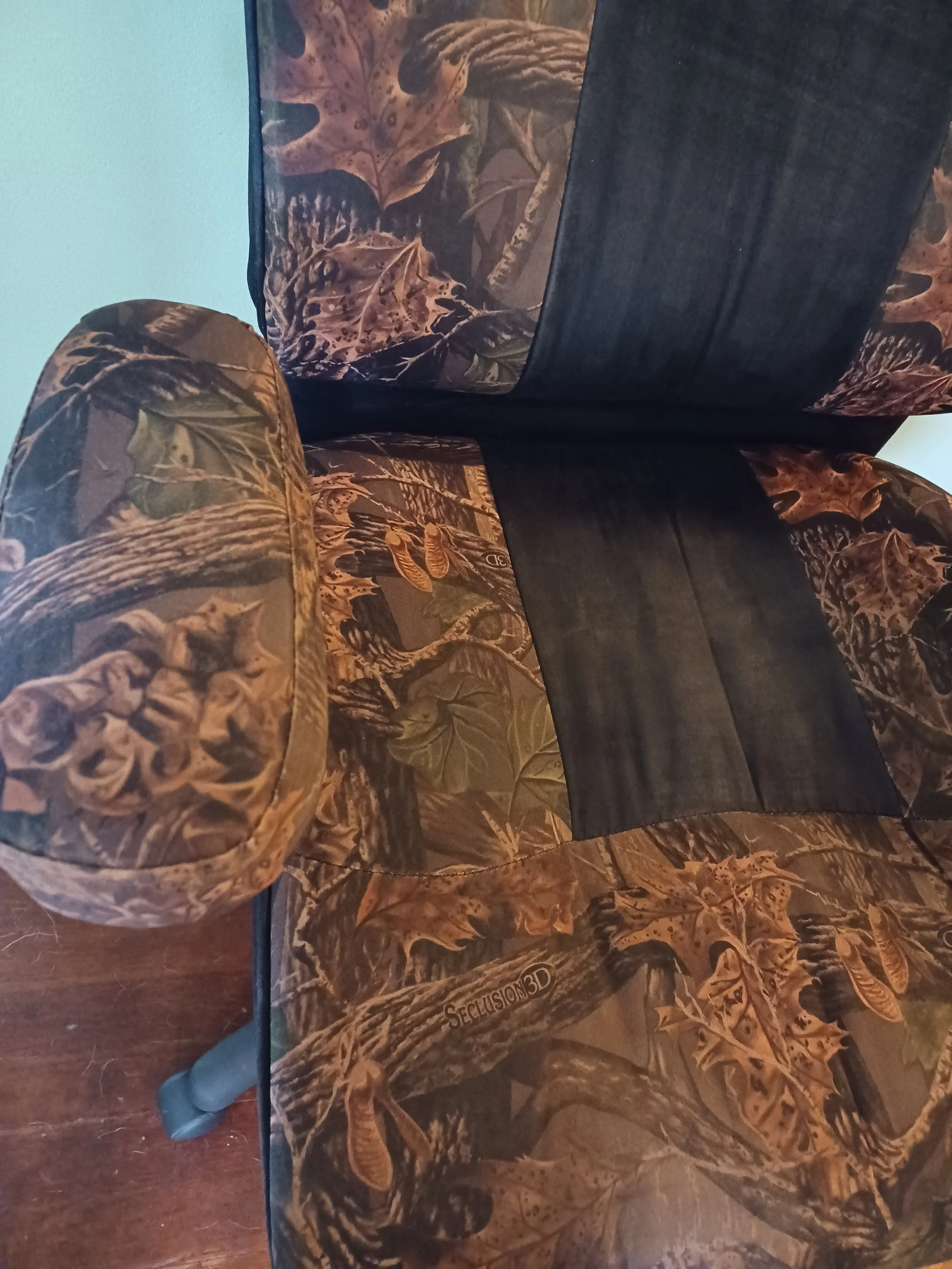A camouflage patterned chair with a matching footrest on a wooden floor, and a blue wall in the background. Visibly Clean