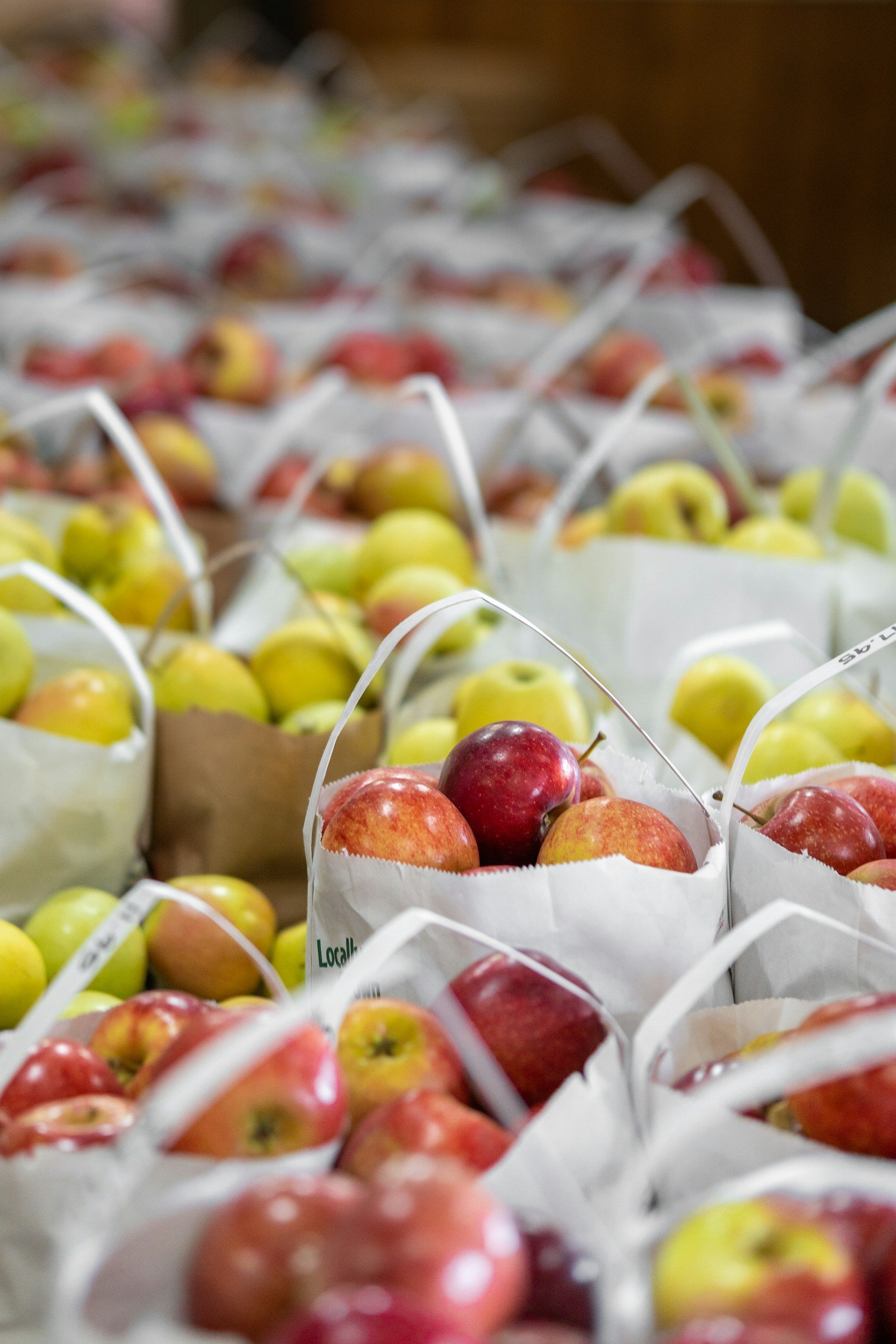 Close-up view of multiple small paper bags filled with red and yellow apples, stacked on a surface, with some bags partially overlapping.